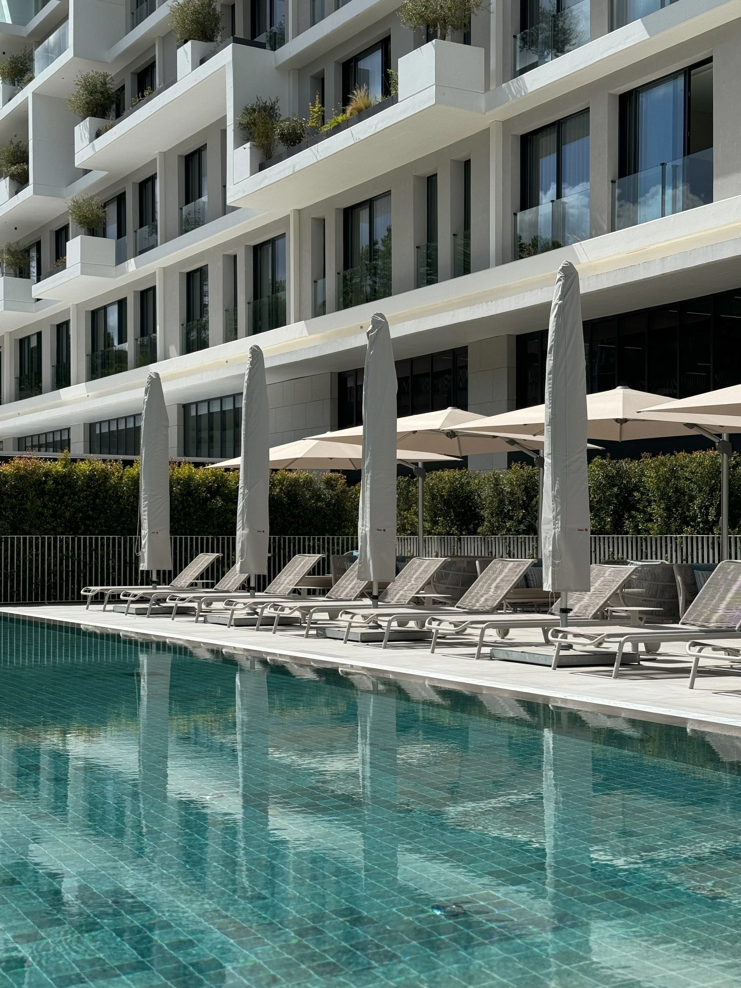 Outdoor pool with sun loungers and umbrellas set against sleek modern architecture, perfect for relaxation in Lisbon, Martinhal Lisbon Oriente – Lisbon, Portugal.