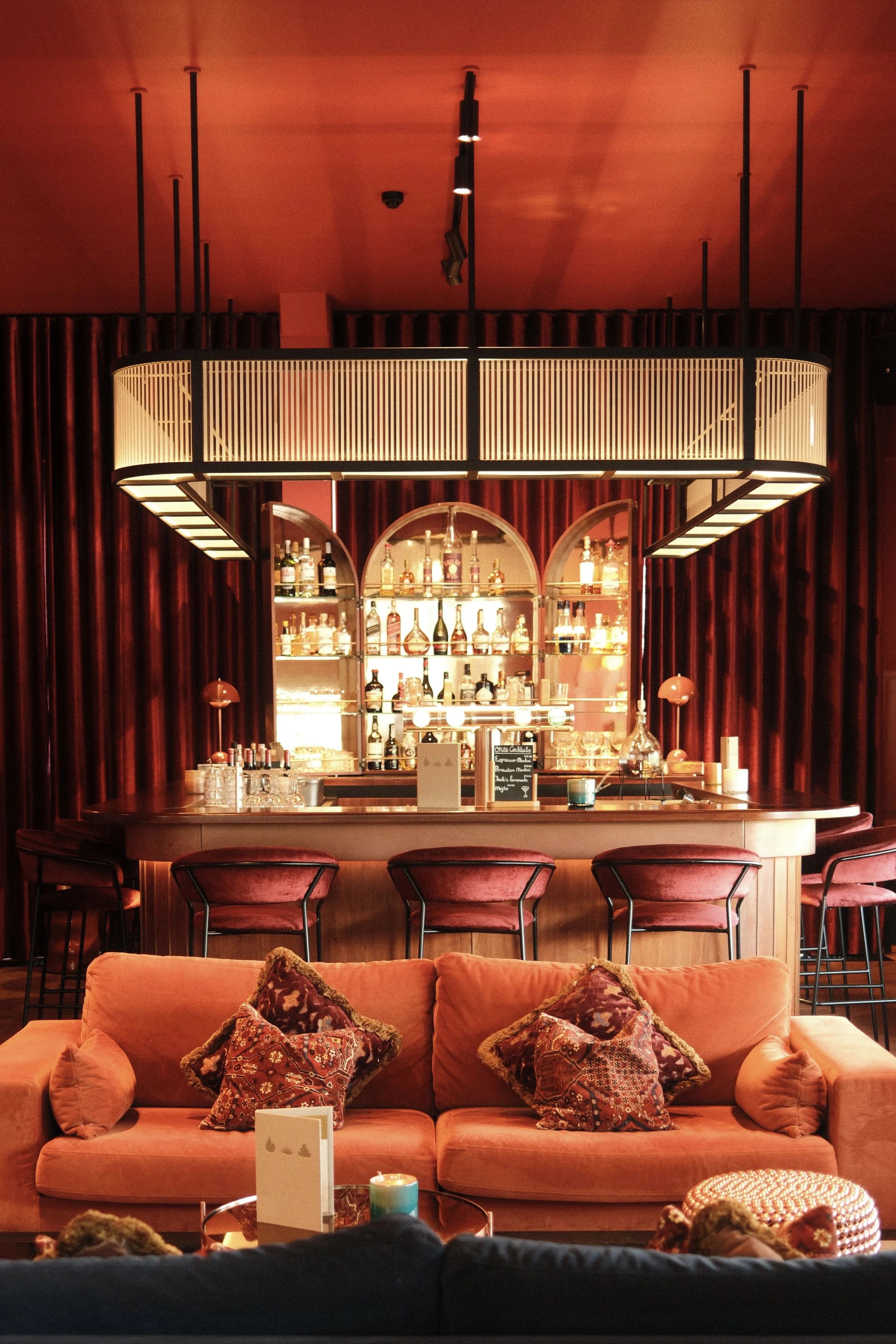 Stylish bar with red tones, plush seating, and illuminated shelves showcasing curated spirits, Château St. Gerlach – Vaeshartelt Maastricht.
