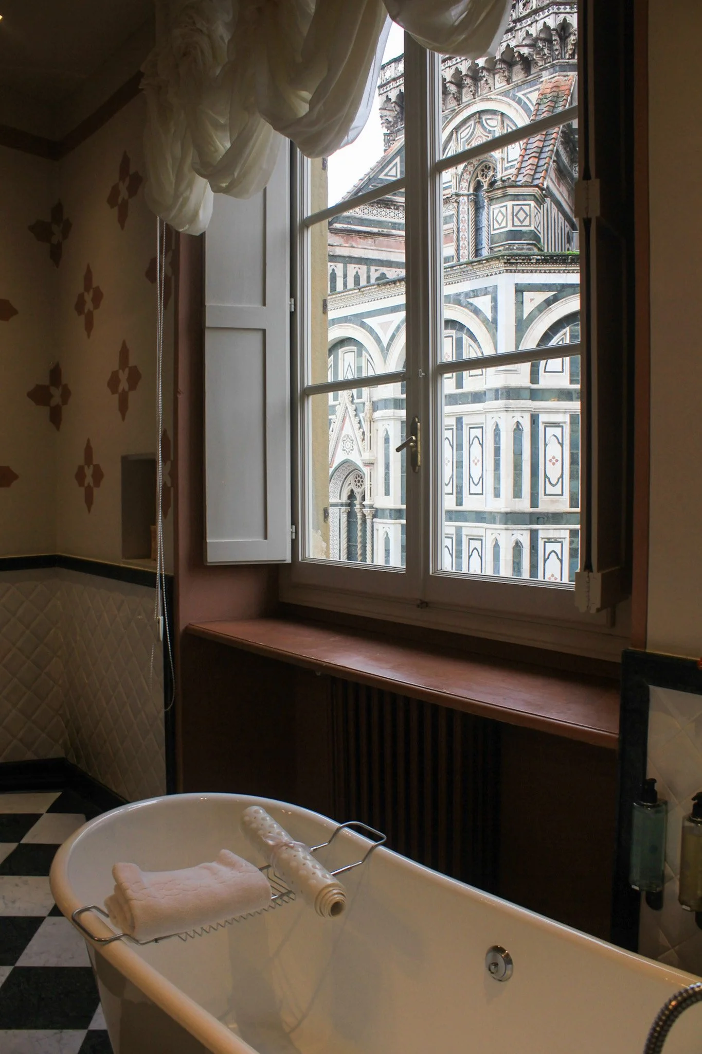 Freestanding bathtub with Duomo views through tall window in elegant palace bathroom, Palazzo Niccolini al Duomo – Florence, Italy.