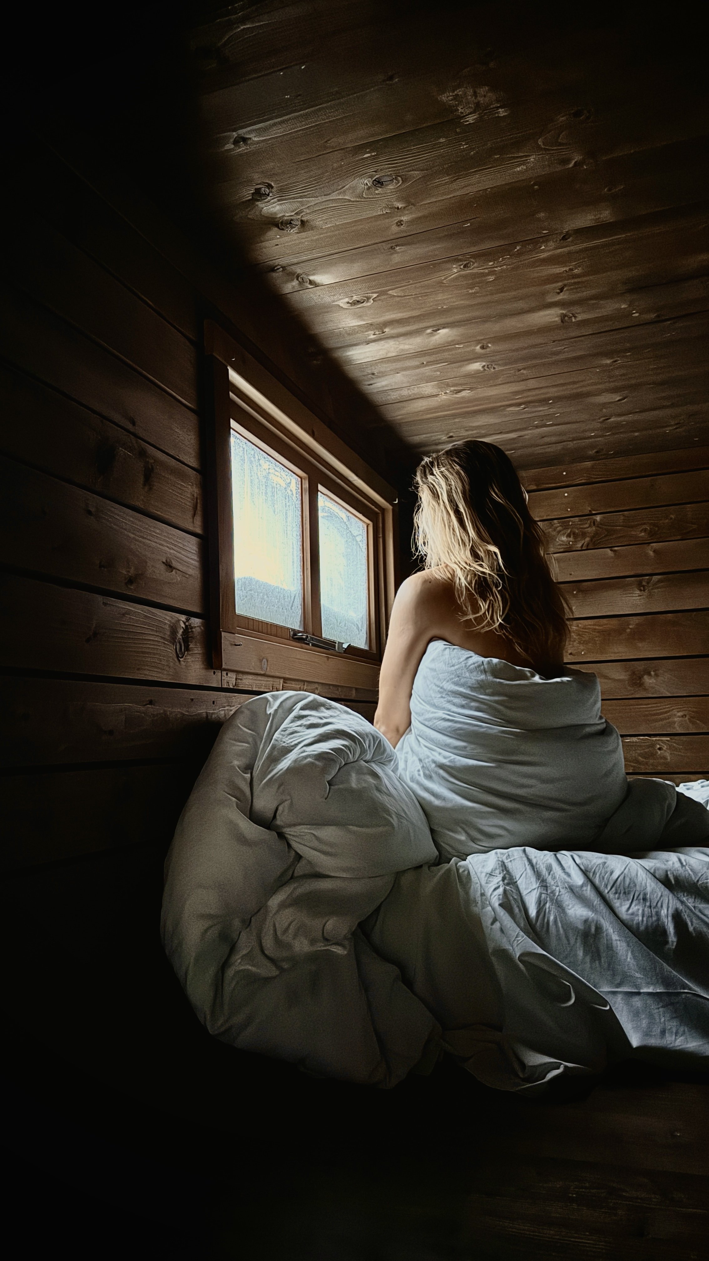 A quiet moment on a wooden bed facing a small window, wrapped in blankets and winter light, Nutchel Forest Village Alsace – Plaine, France.
