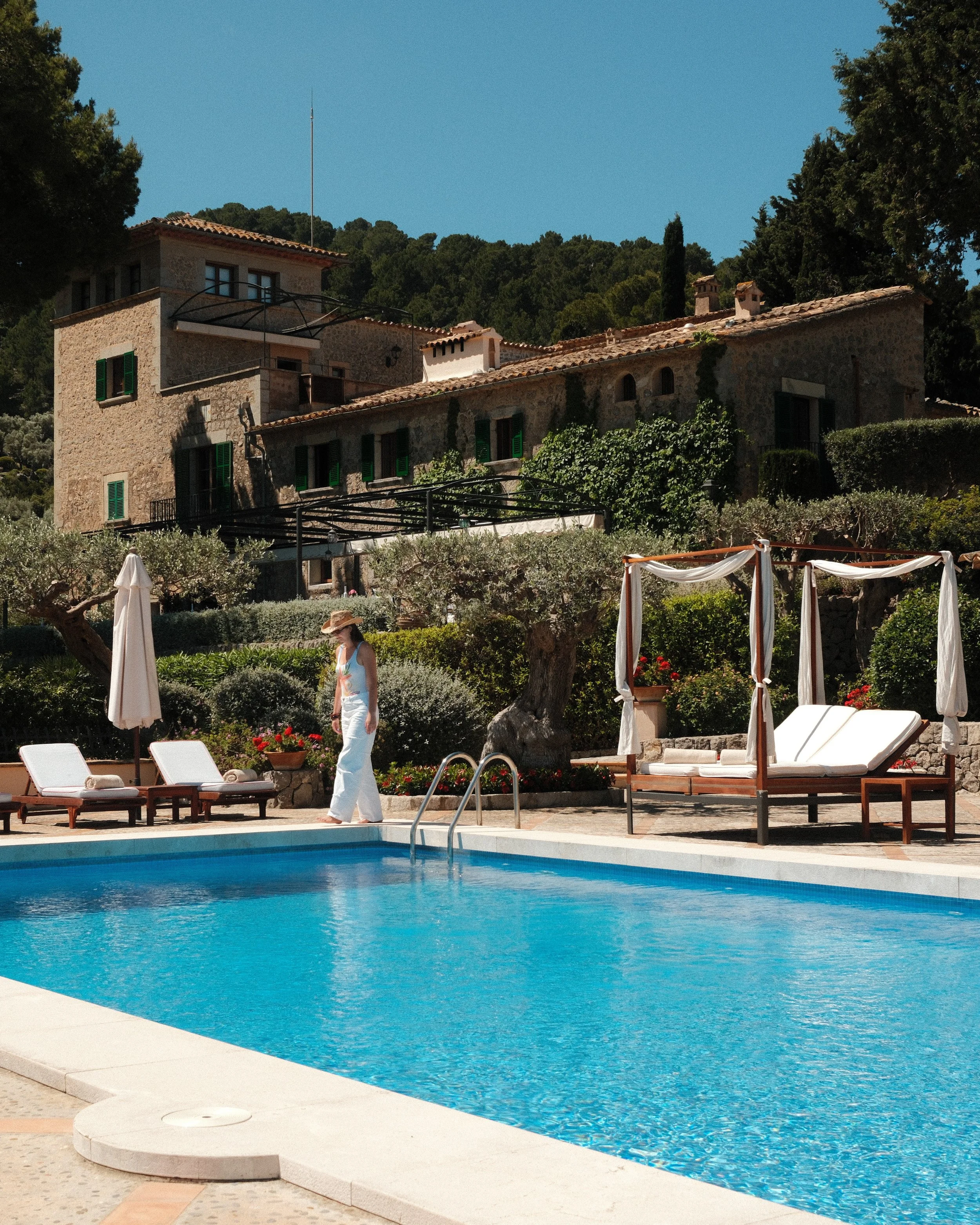 Pool terrace framed by olive trees and a restored stone manor house at Sa Pedrissa overlooking the Tramuntana mountains, Mallorca, Spain