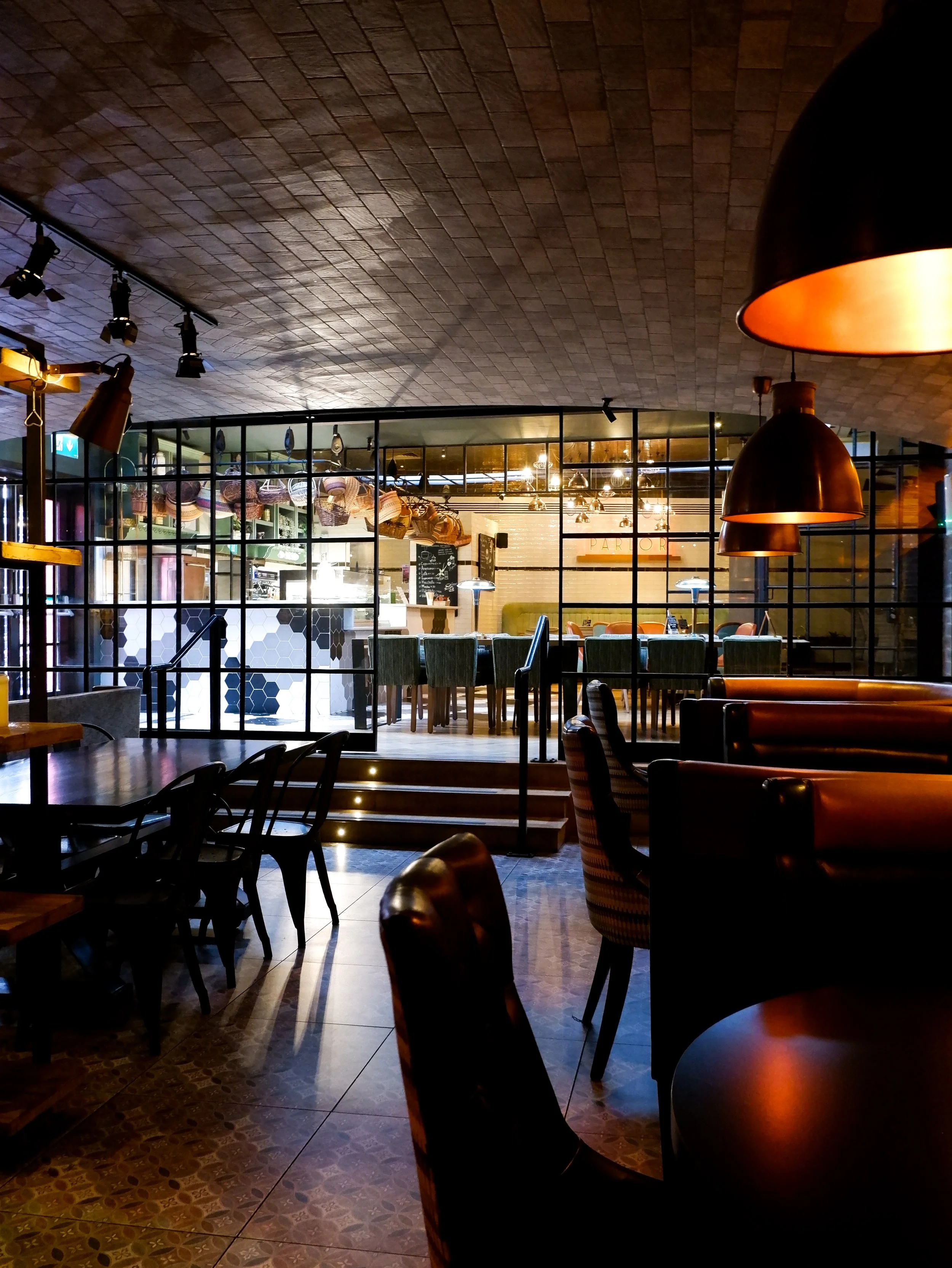 Contemporary dining and lounge area with warm lighting, leather seating, and an open kitchen behind glass partitions