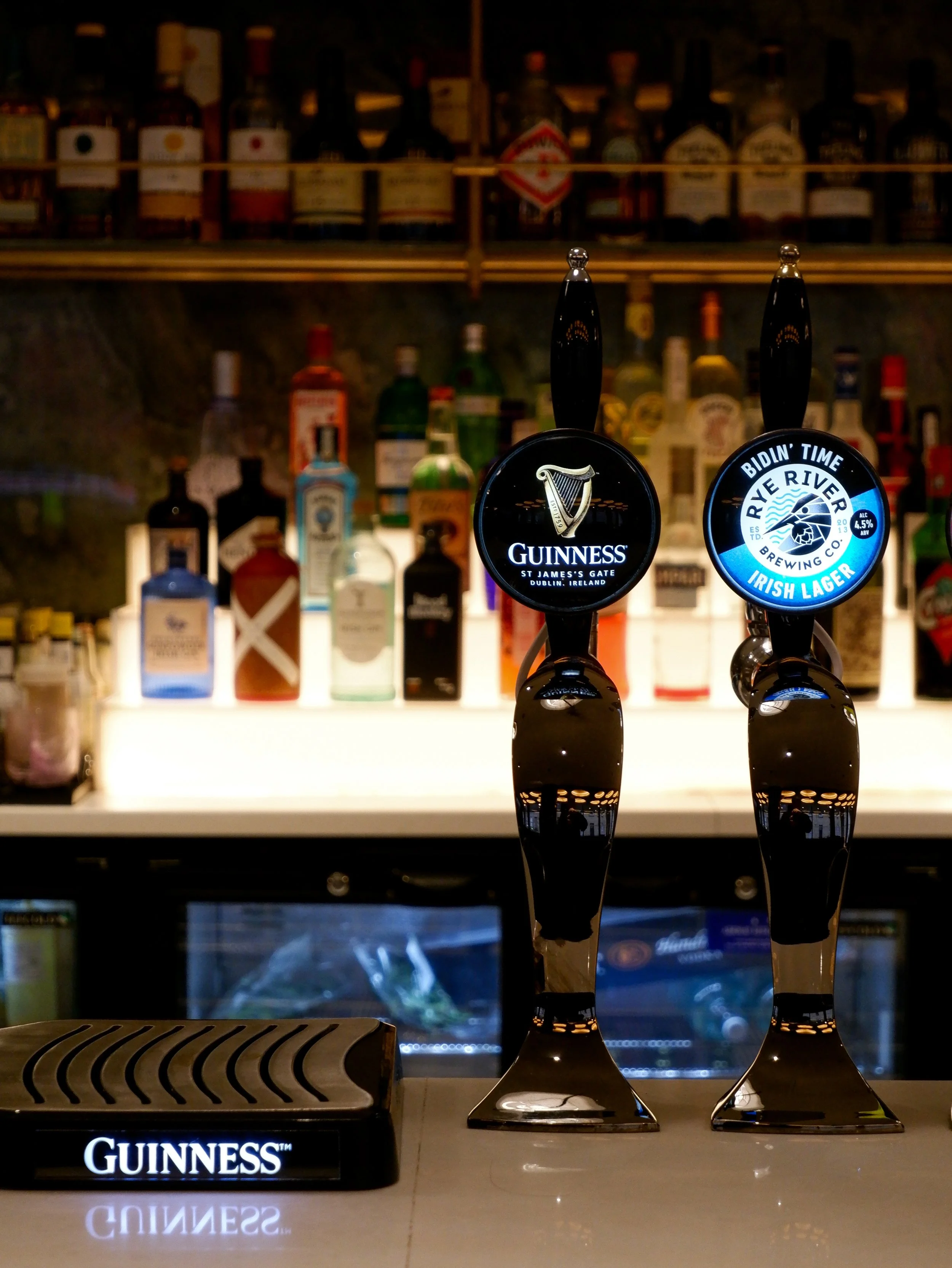 Guinness and Rye River beer taps displayed against an illuminated bar stocked with premium spirits