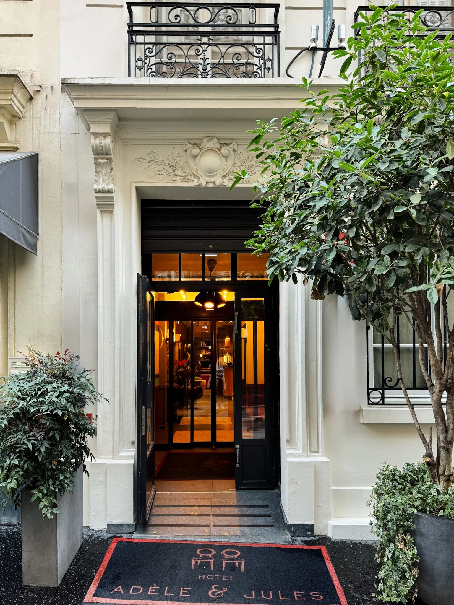 Boutique hotel entrance framed by classic Parisian architecture and greenery