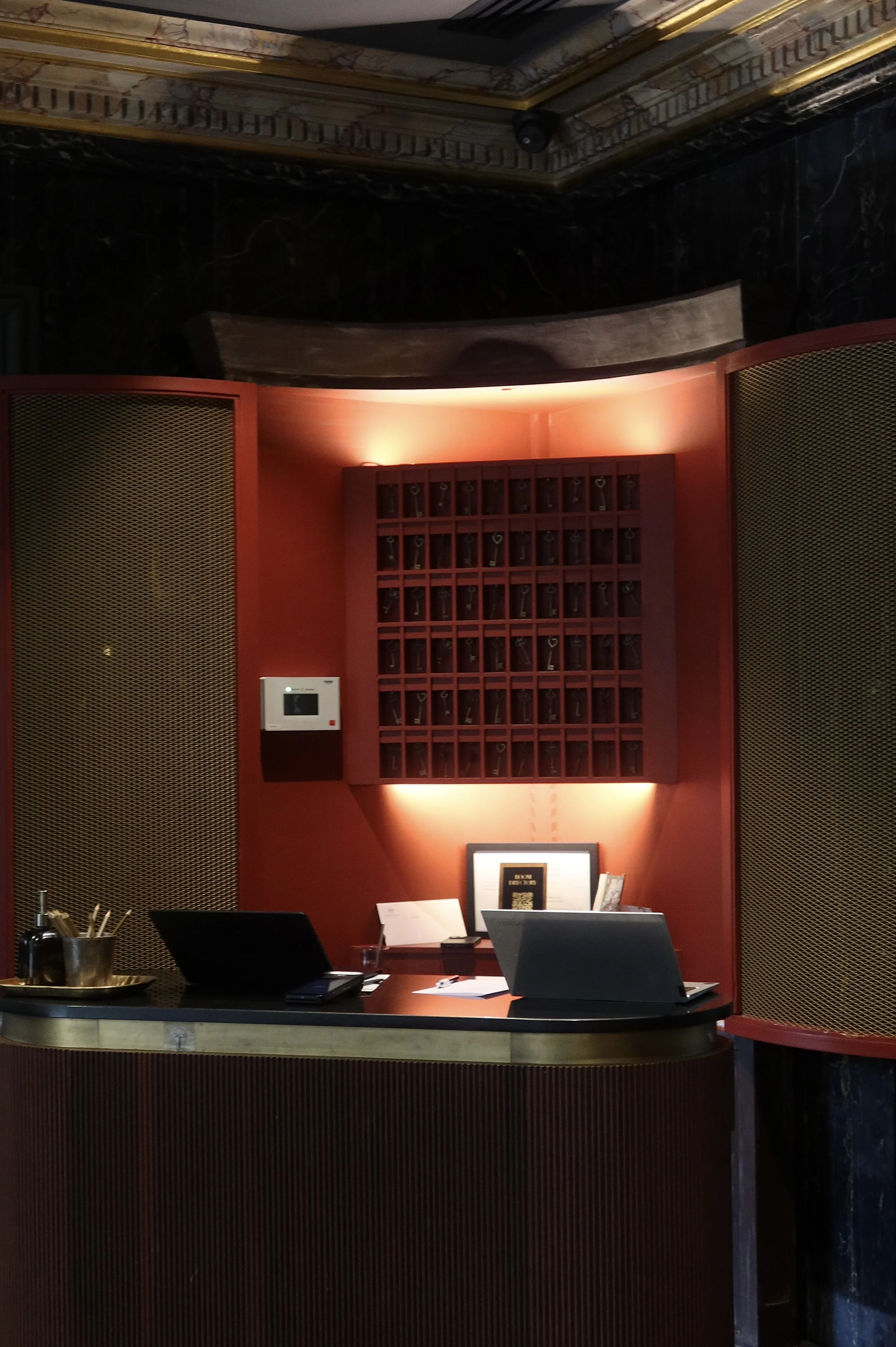 Boutique reception desk framed by deep red walls, brass details, and vintage key storage display, Victoria Palace Hotel – Paris, France.