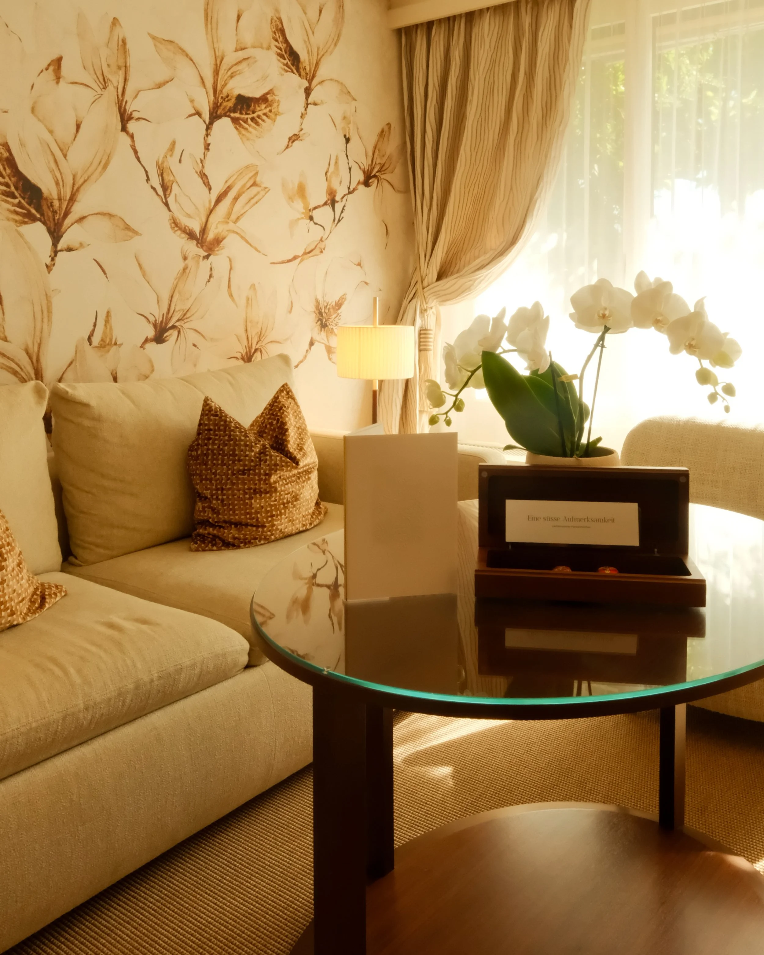 Bright lounge area with floral wallpaper, orchids, and elegant furnishings