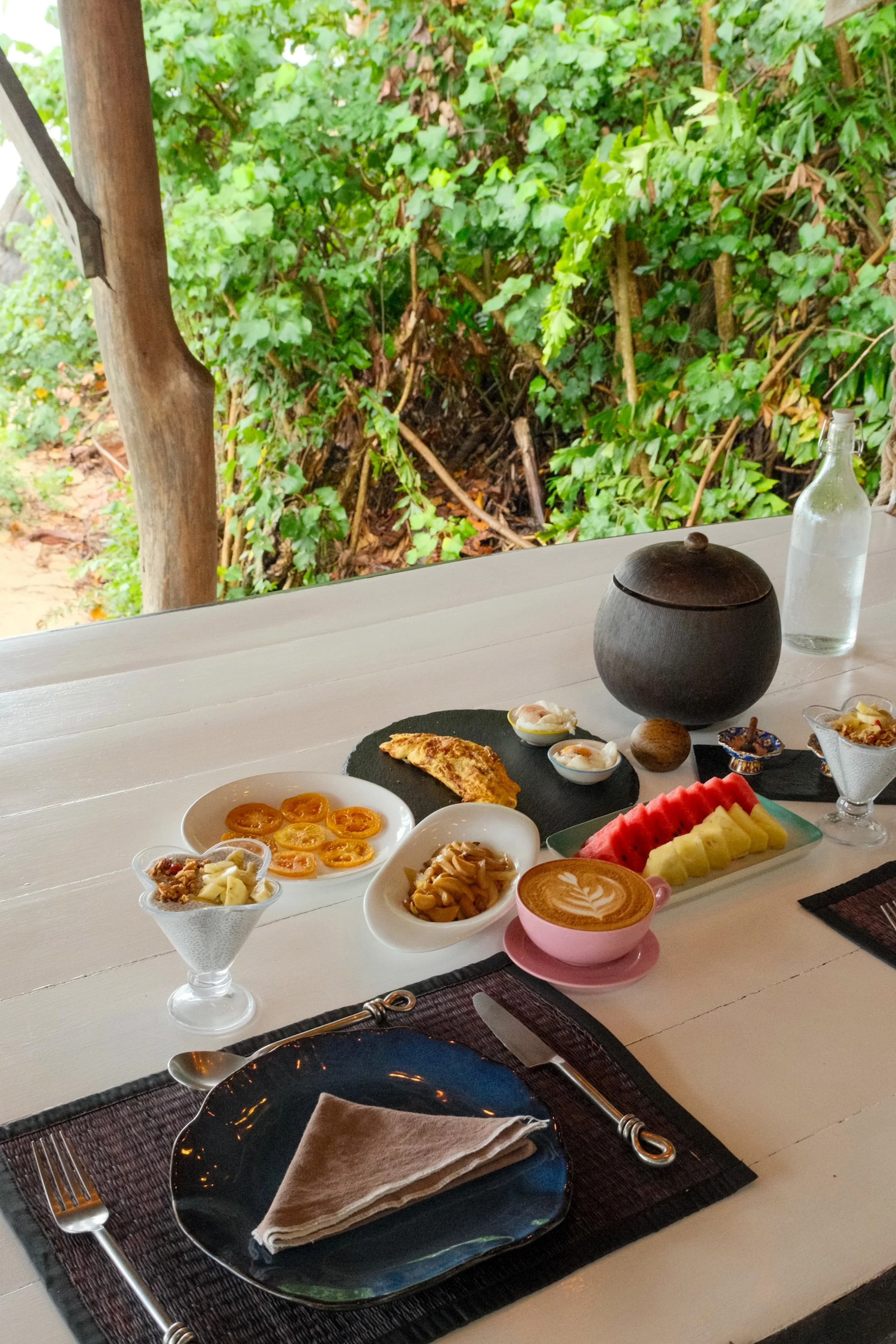 Breakfast spread with tropical fruit, yogurt, eggs, coffee, and fresh dishes served beside lush island greenery