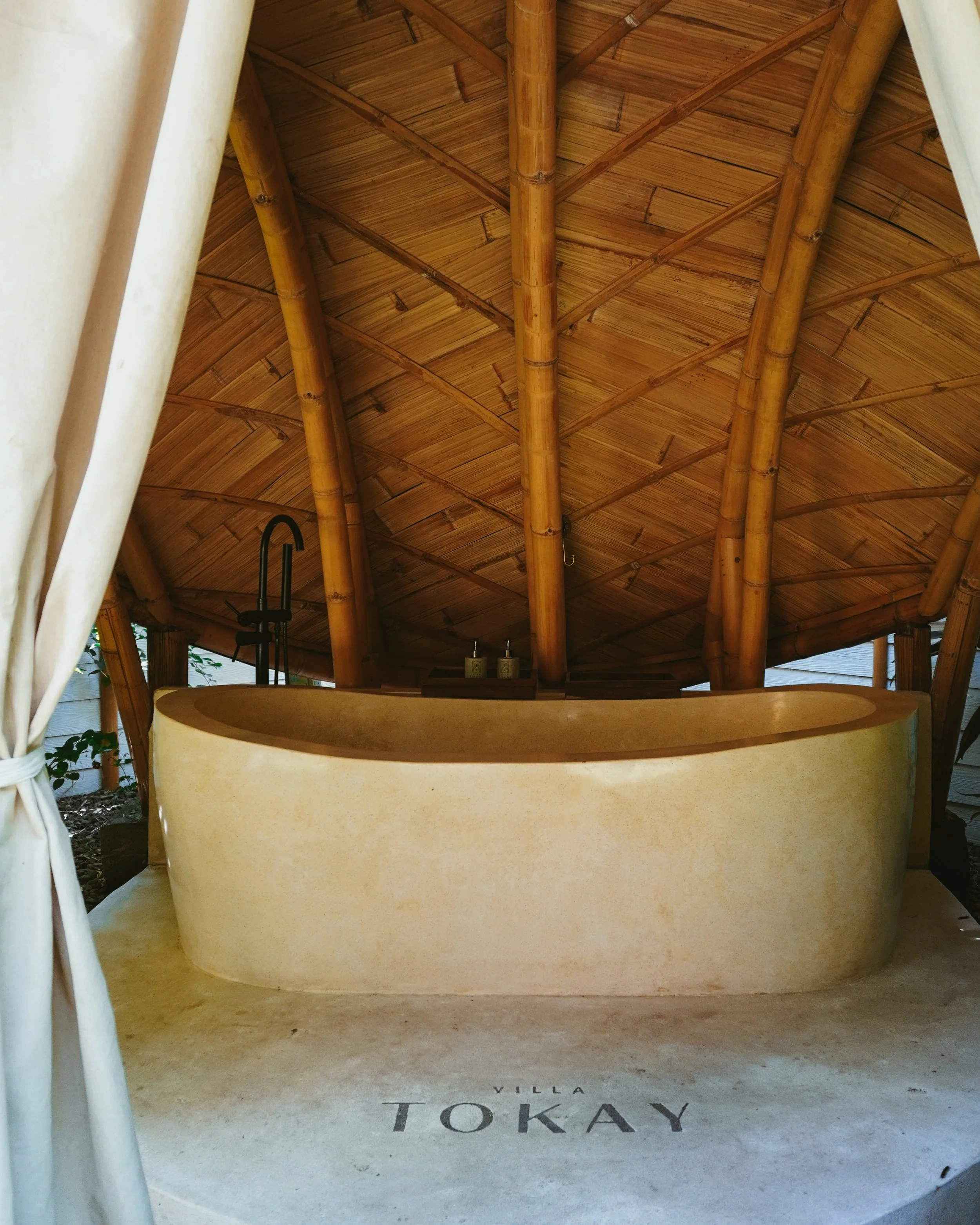 An open air stone bathtub sits beneath a handcrafted bamboo canopy