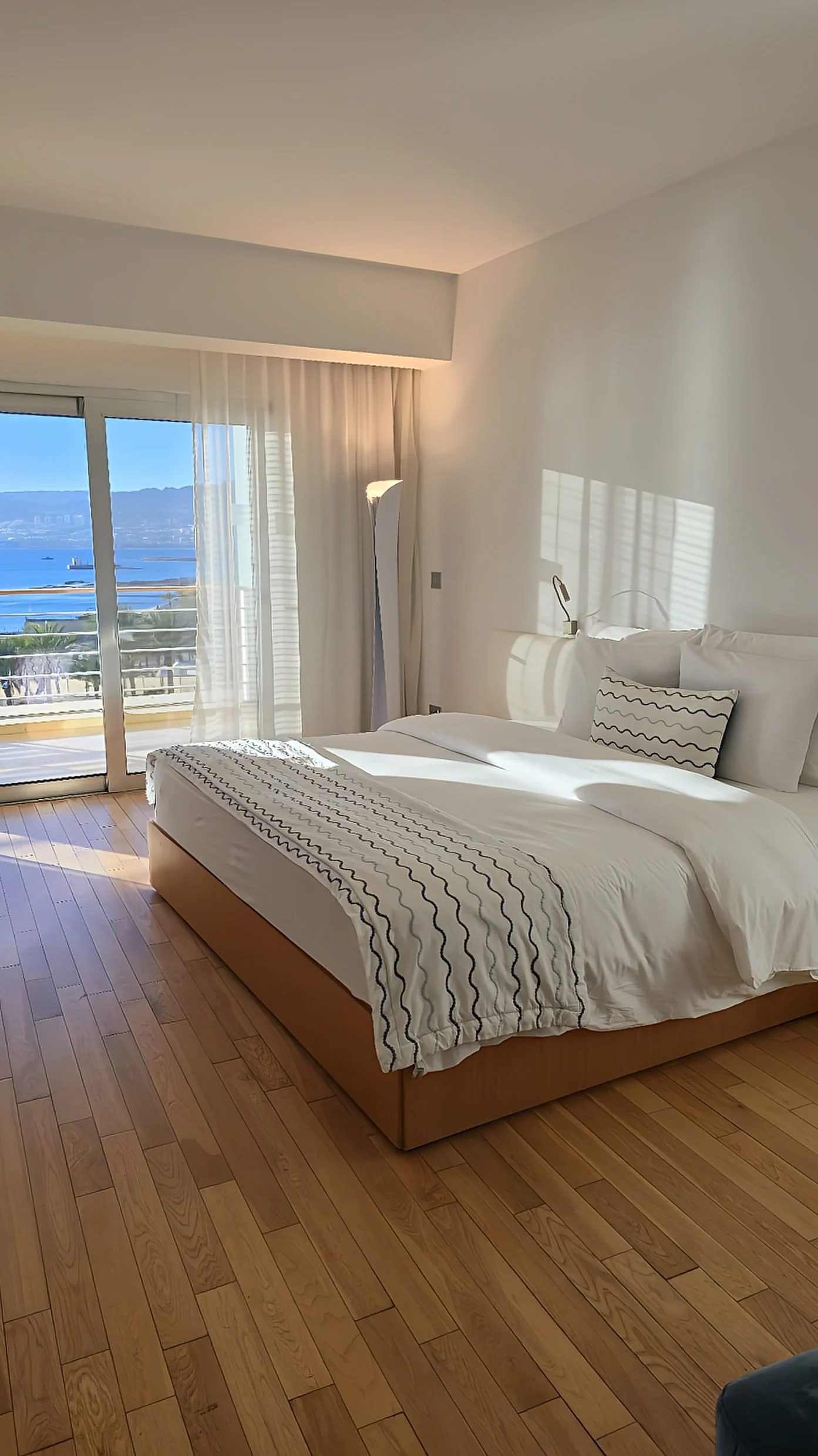 Bright sea-view bedroom with floor-to-ceiling windows, wooden floors, and soft morning light overlooking the Red Sea, Kempinski Hotel Aqaba Red Sea – Aqaba, Jordan.