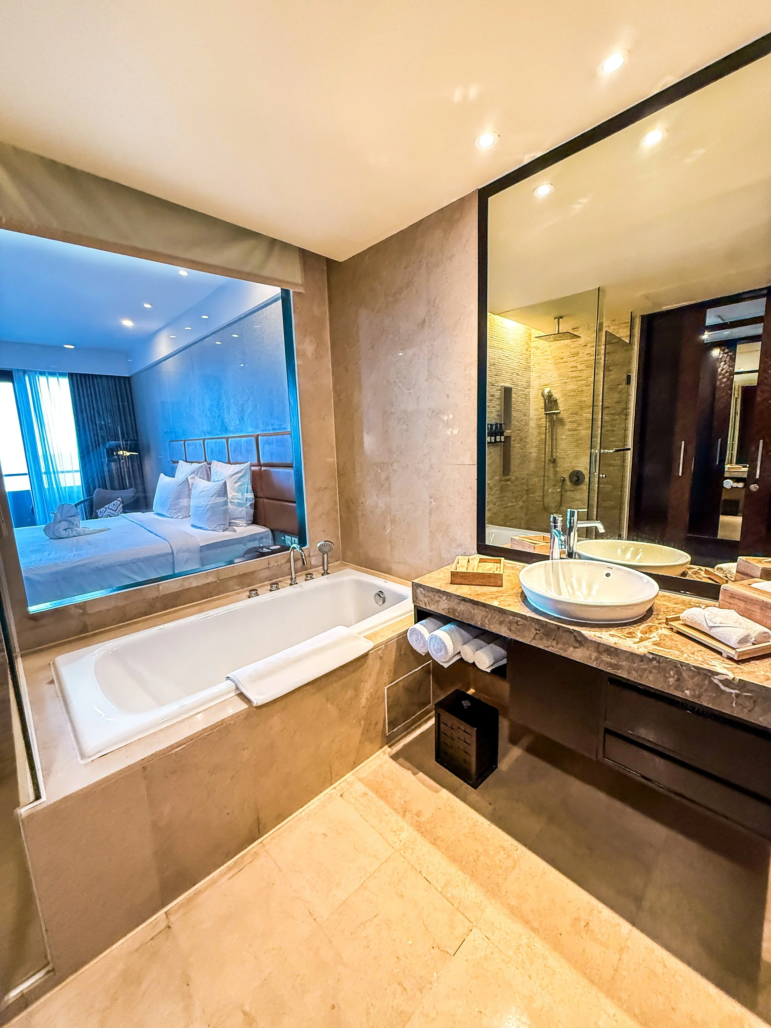 The spacious bathroom combines a soaking bathtub, rain shower, marble finishes, and modern design