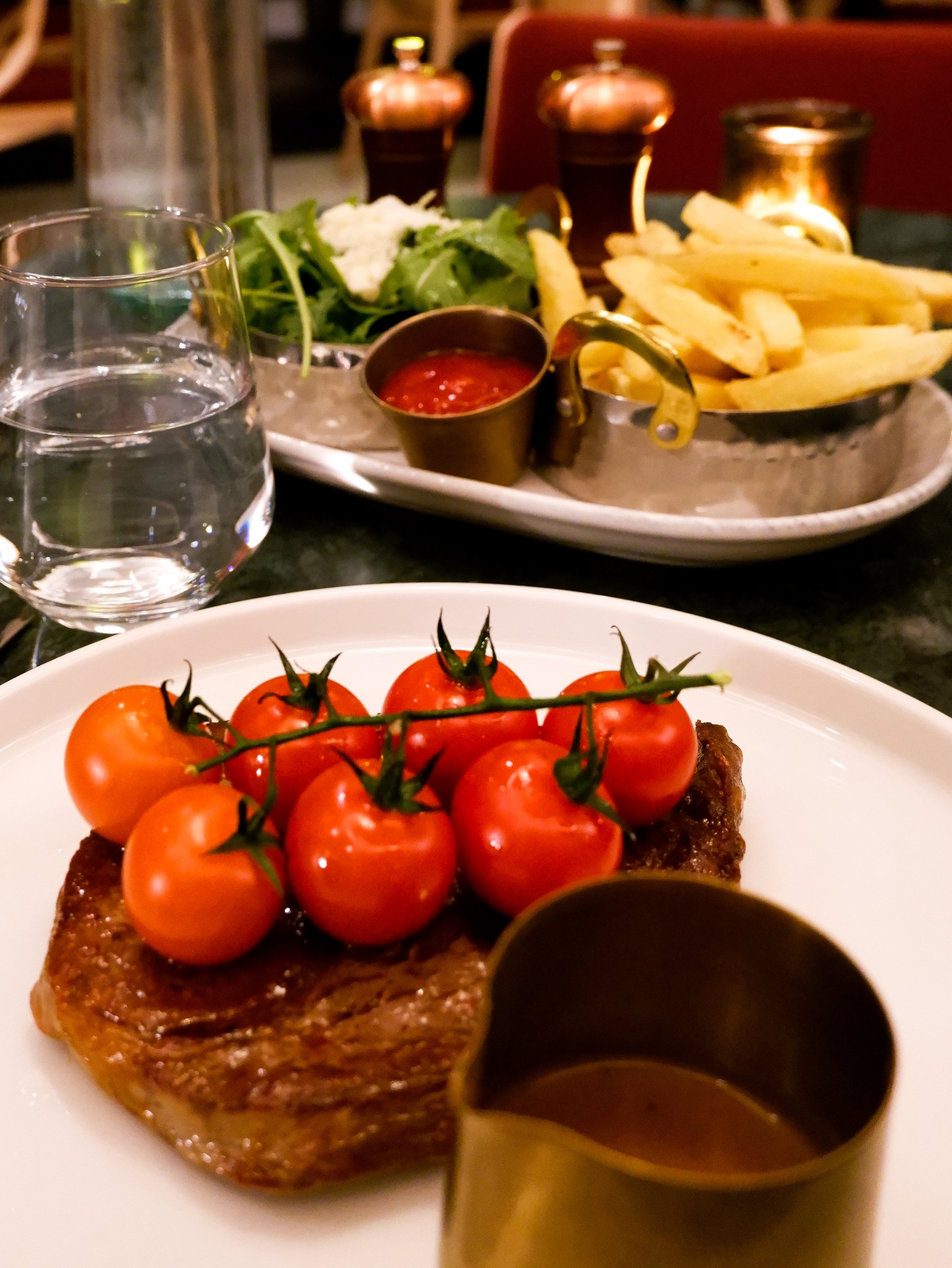 Grilled steak topped with cherry tomatoes, served with golden fries, fresh greens, and sauce
