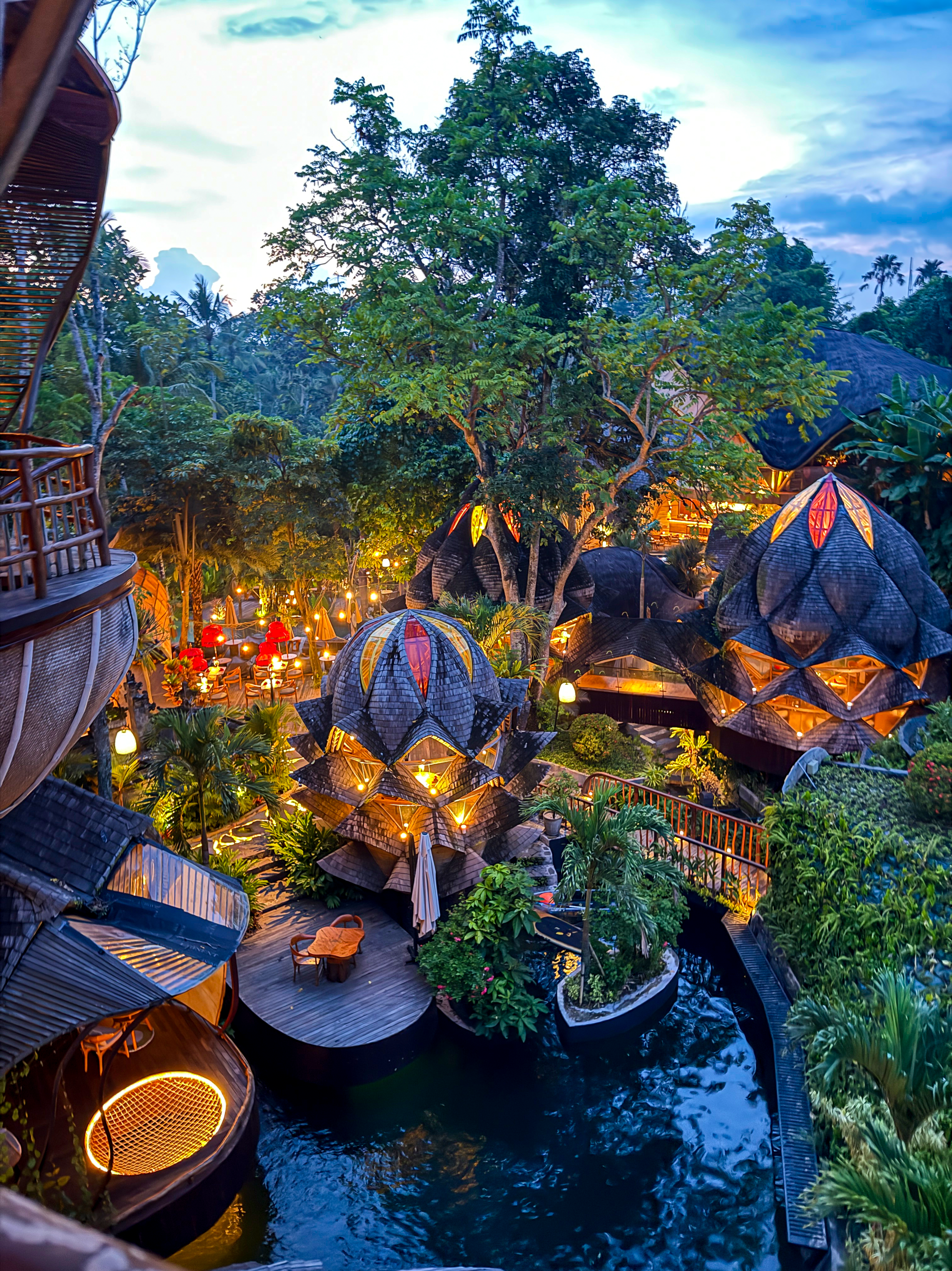 An evening view reveals illuminated bamboo villas, winding waterways, and lush tropical gardens creating a magical atmosphere after sunset