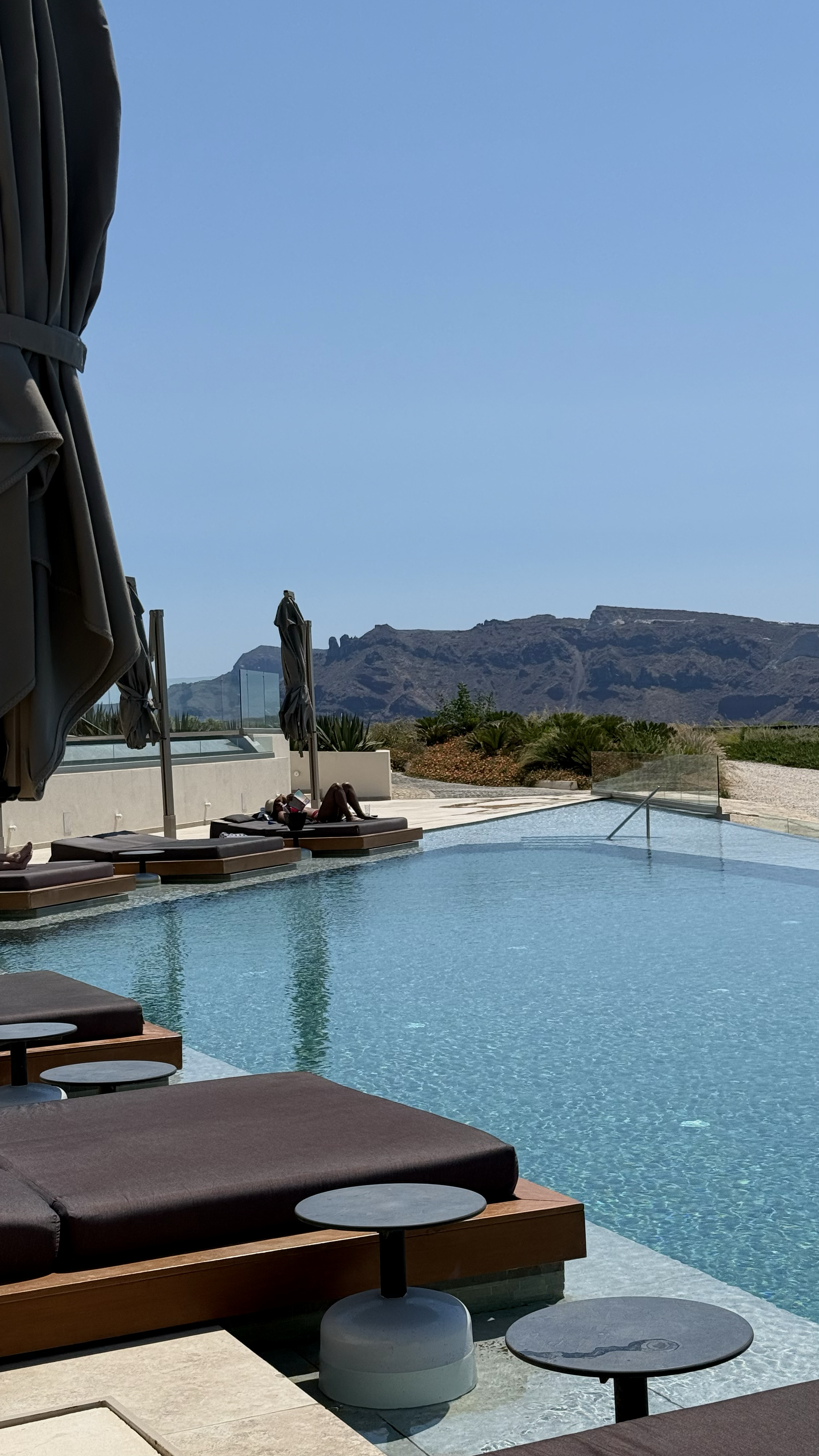 Infinity pool surrounded by contemporary sun loungers overlooking Santorini’s dramatic volcanic landscape