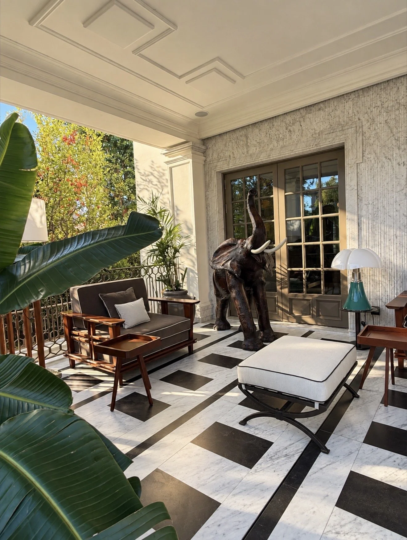Elegant veranda with marble flooring, tropical plants, wooden seating, and a decorative elephant sculpture