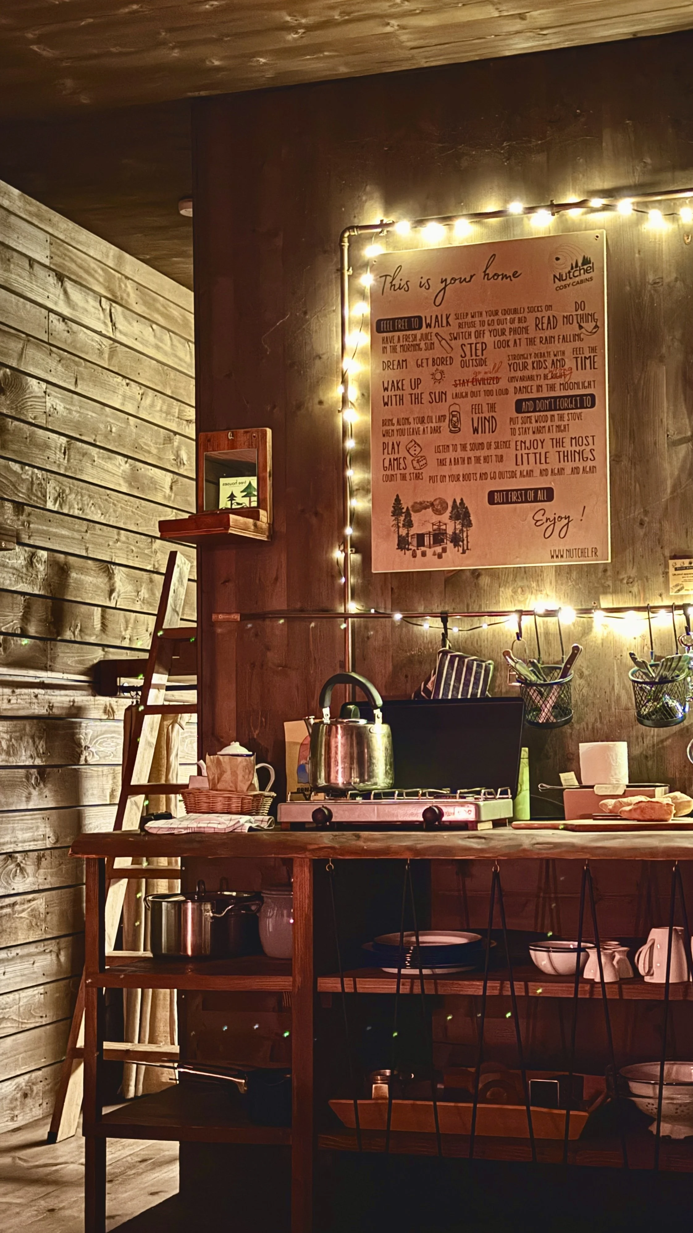 A rustic kitchen corner with open shelves, lantern light, and simple cookware designed for mindful, off-grid living, Nutchel Forest Village Alsace – Plaine, France