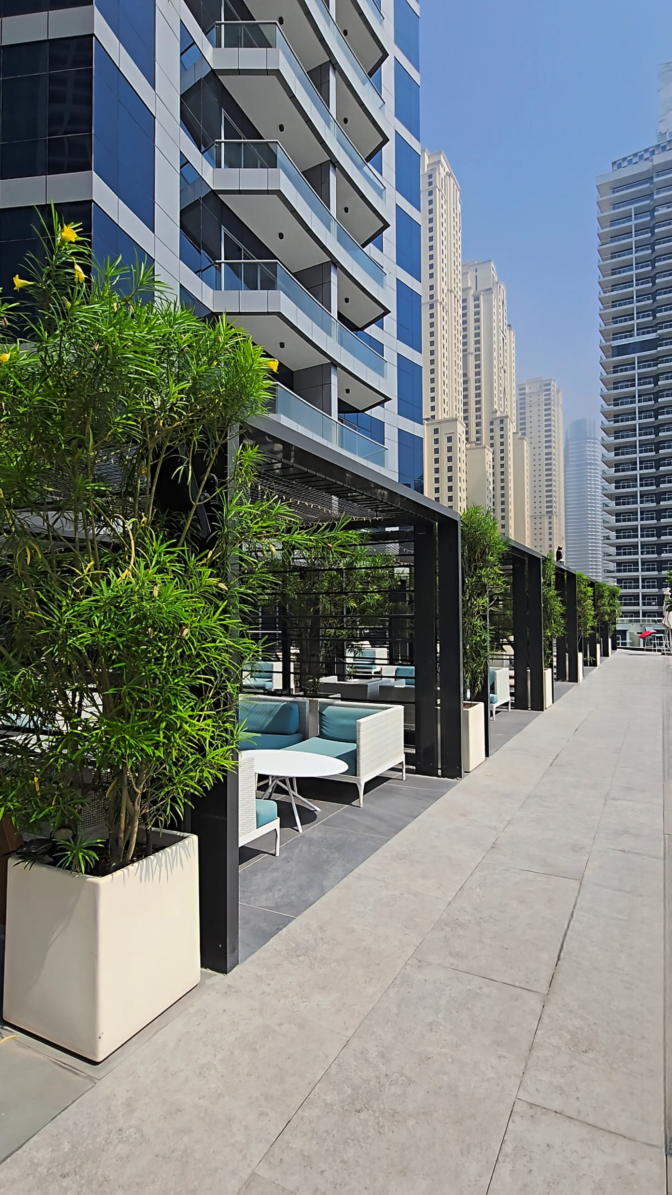 Outdoor terrace featuring private shaded cabanas, turquoise seating, tropical plants, and surrounding skyscrapers