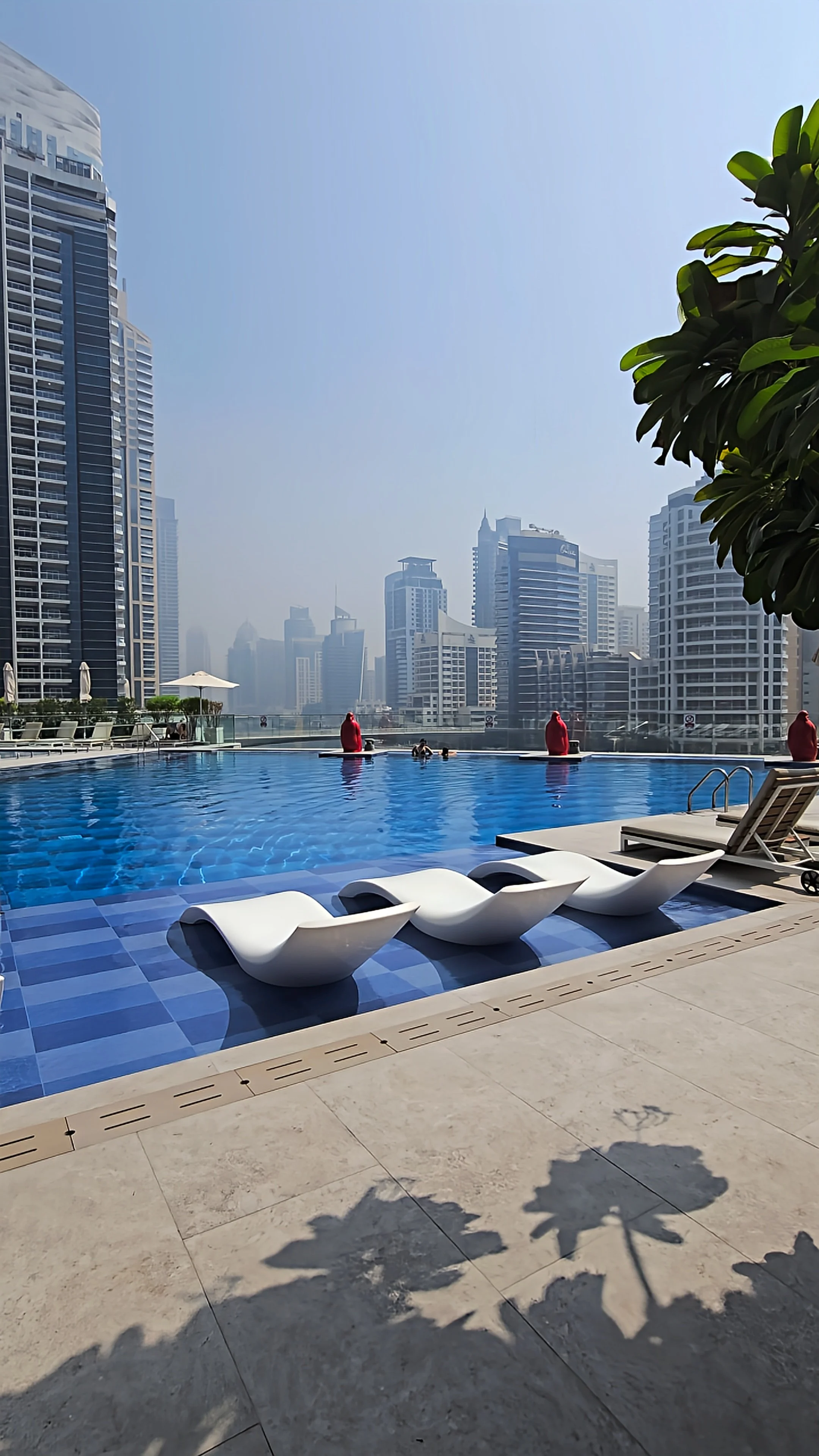 Outdoor swimming pool featuring submerged loungers, a spacious sun terrace, and panoramic views of Dubai Marina's skyline
