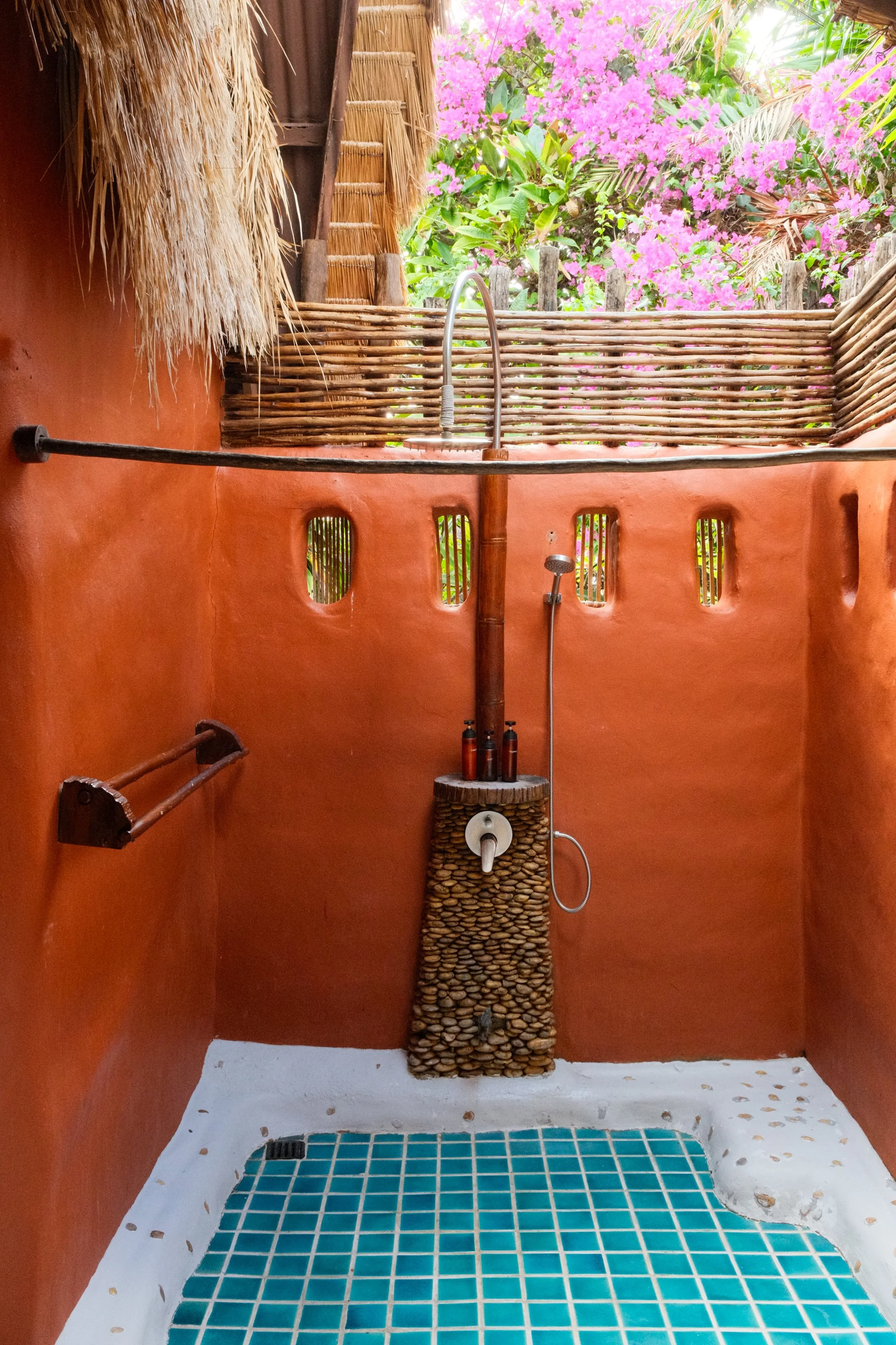 Open-air shower with terracotta walls, turquoise tiles, natural wood, and tropical flowers