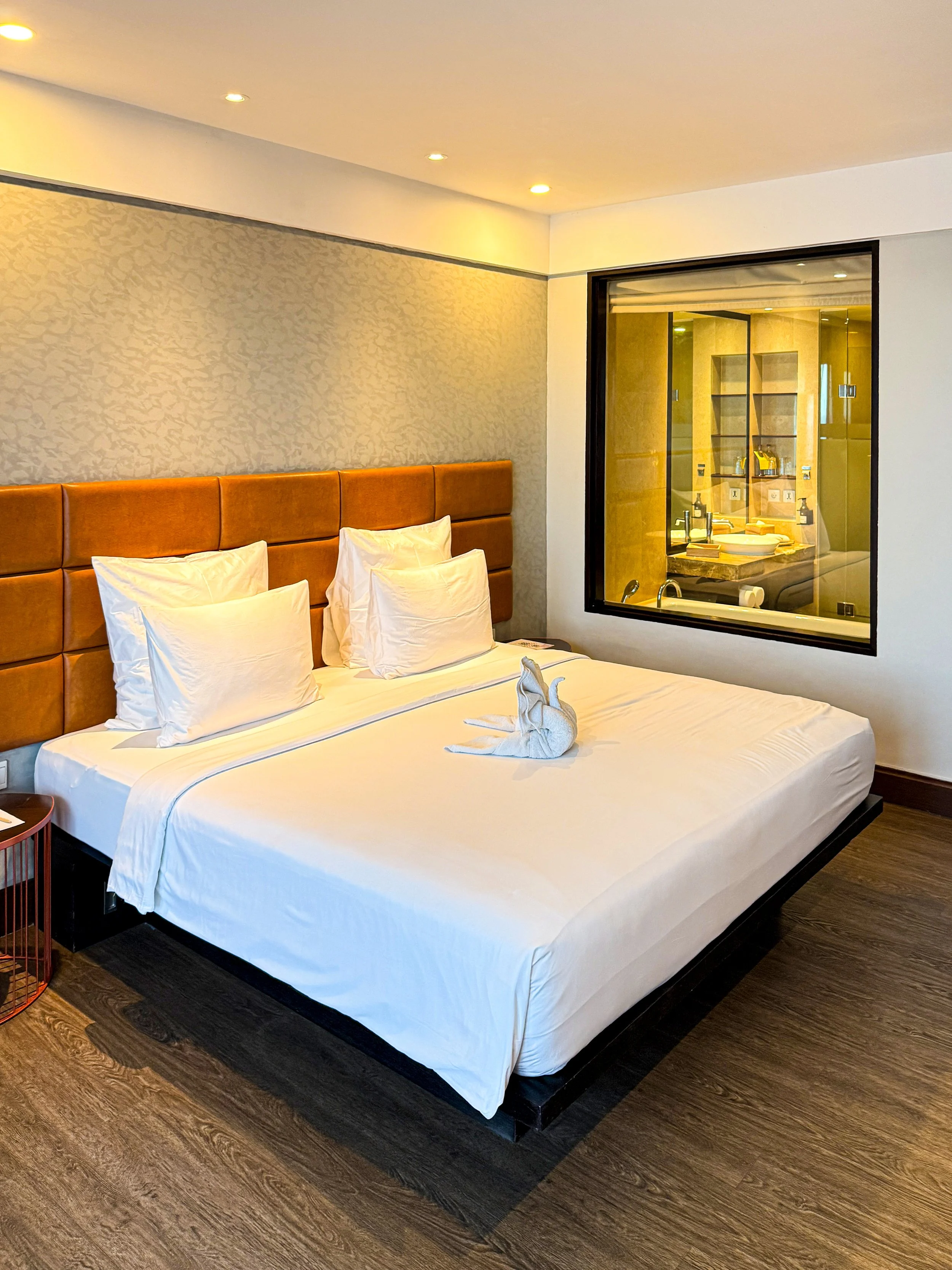 A contemporary guest room features a king bed, warm neutral interiors, and views into the elegant bathroom