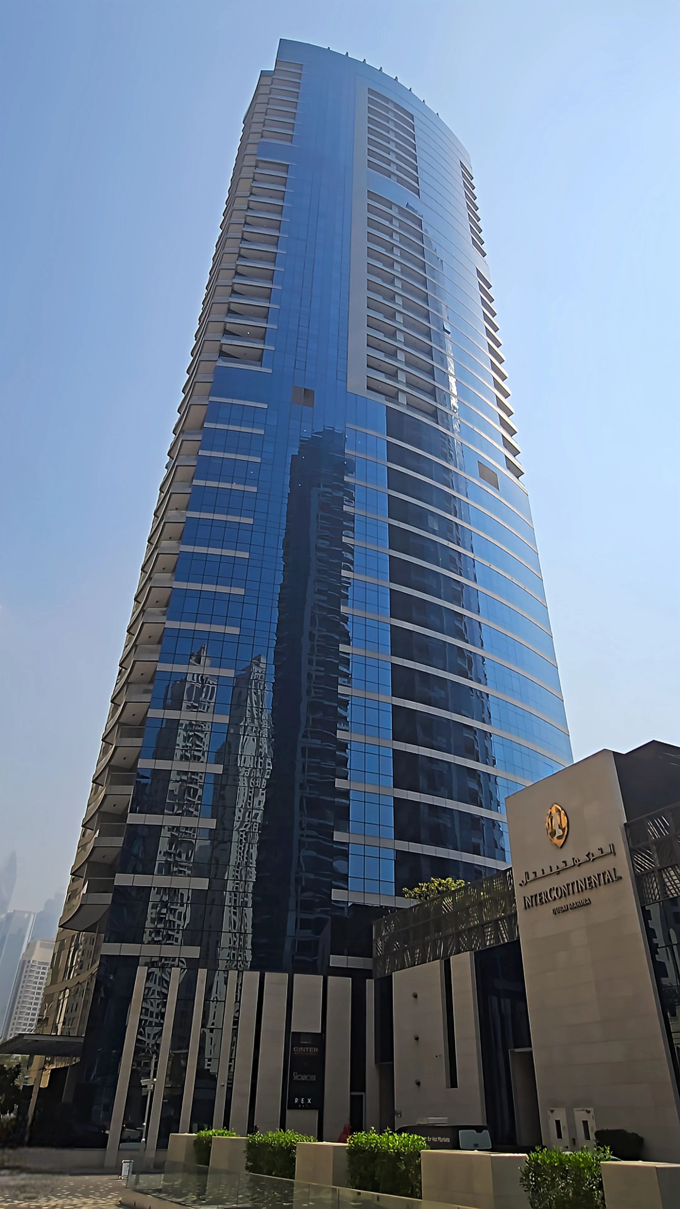Modern hotel exterior featuring a curved blue glass skyscraper, private balconies, and the main entrance