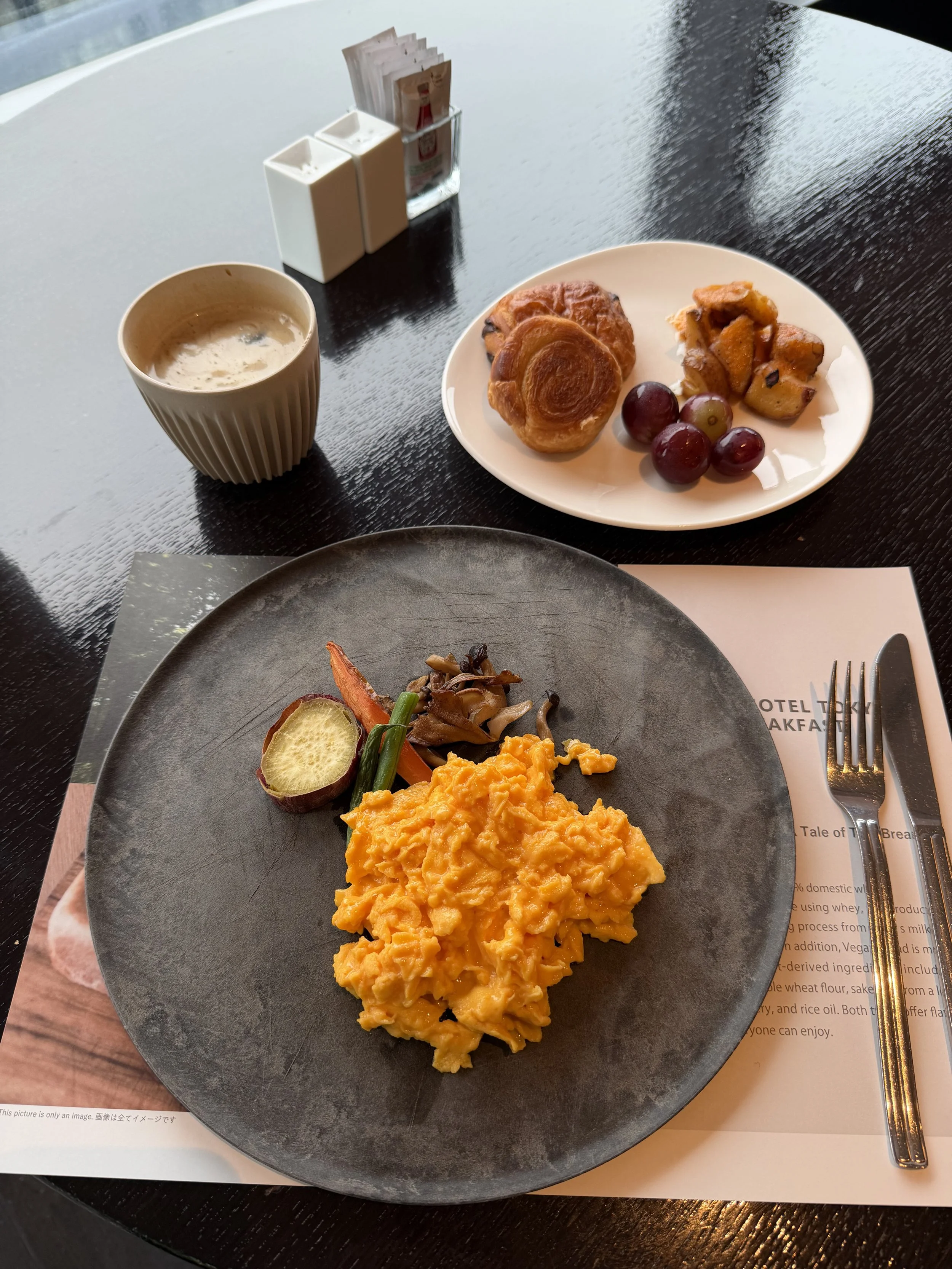 Japanese breakfast with scrambled eggs, roasted vegetables, pastries, fruit, and coffee