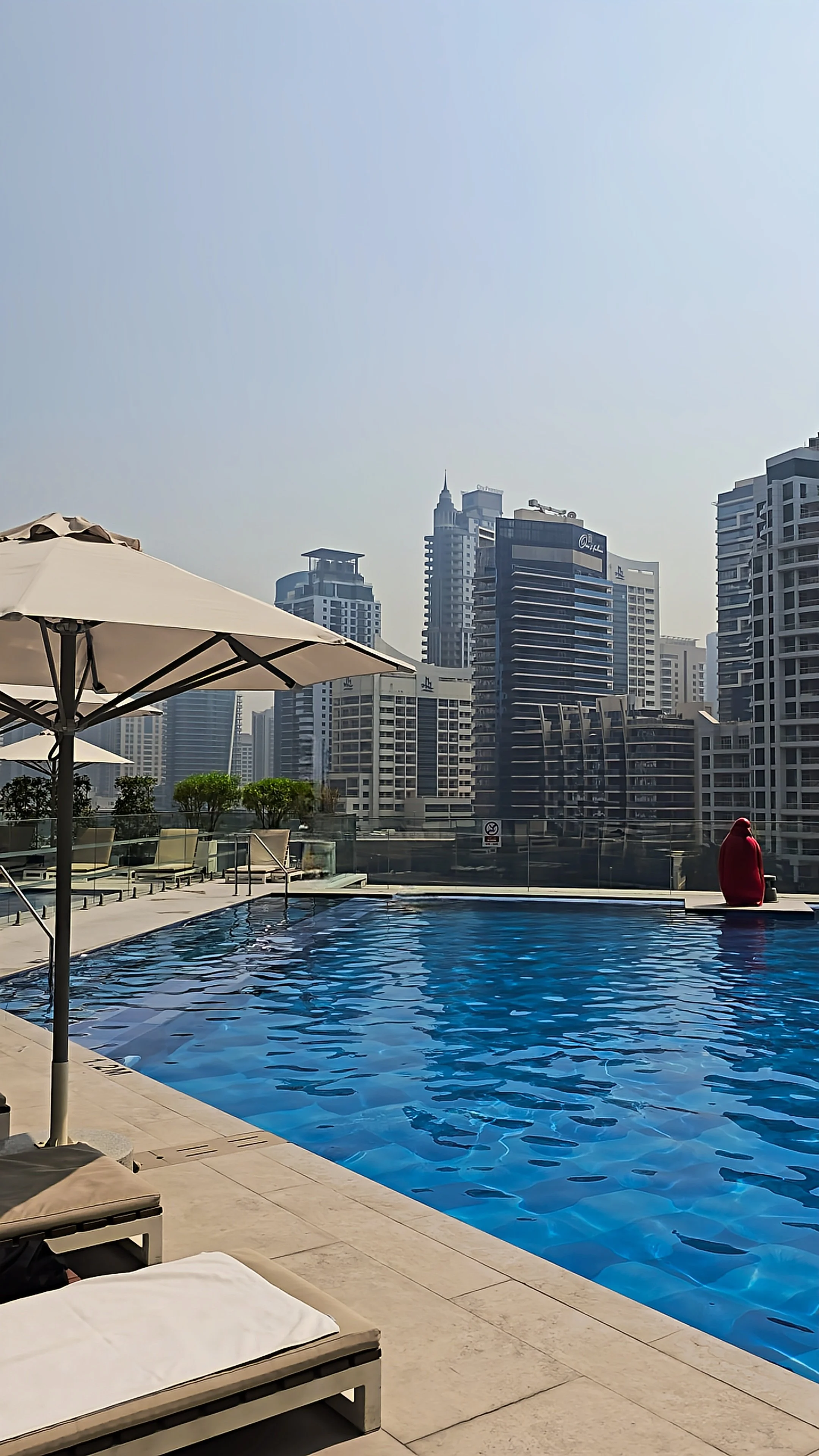 Outdoor swimming pool surrounded by sun loungers, shaded umbrellas, and panoramic views of Dubai's modern skyline
