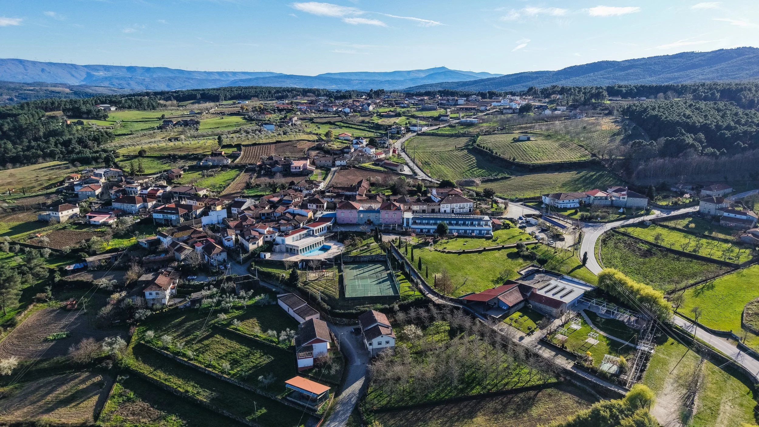Aerial view of a charming countryside village with terracotta rooftops surrounded by green fields and rolling hills, Casas Novas Countryside Hotel Spa & Events – Chaves, Portugal.