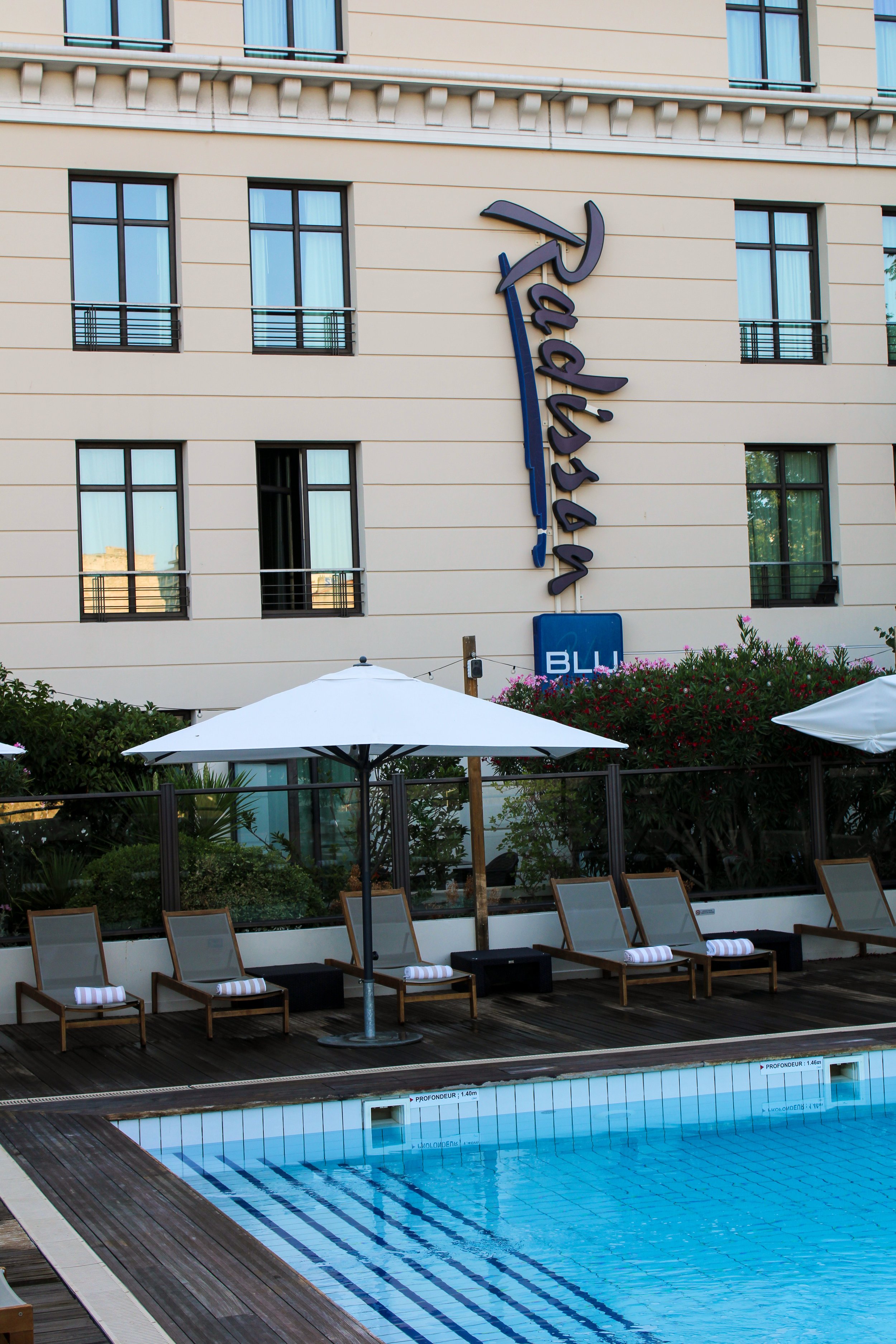 Outdoor pool terrace with sun loungers beside the elegant hotel façade