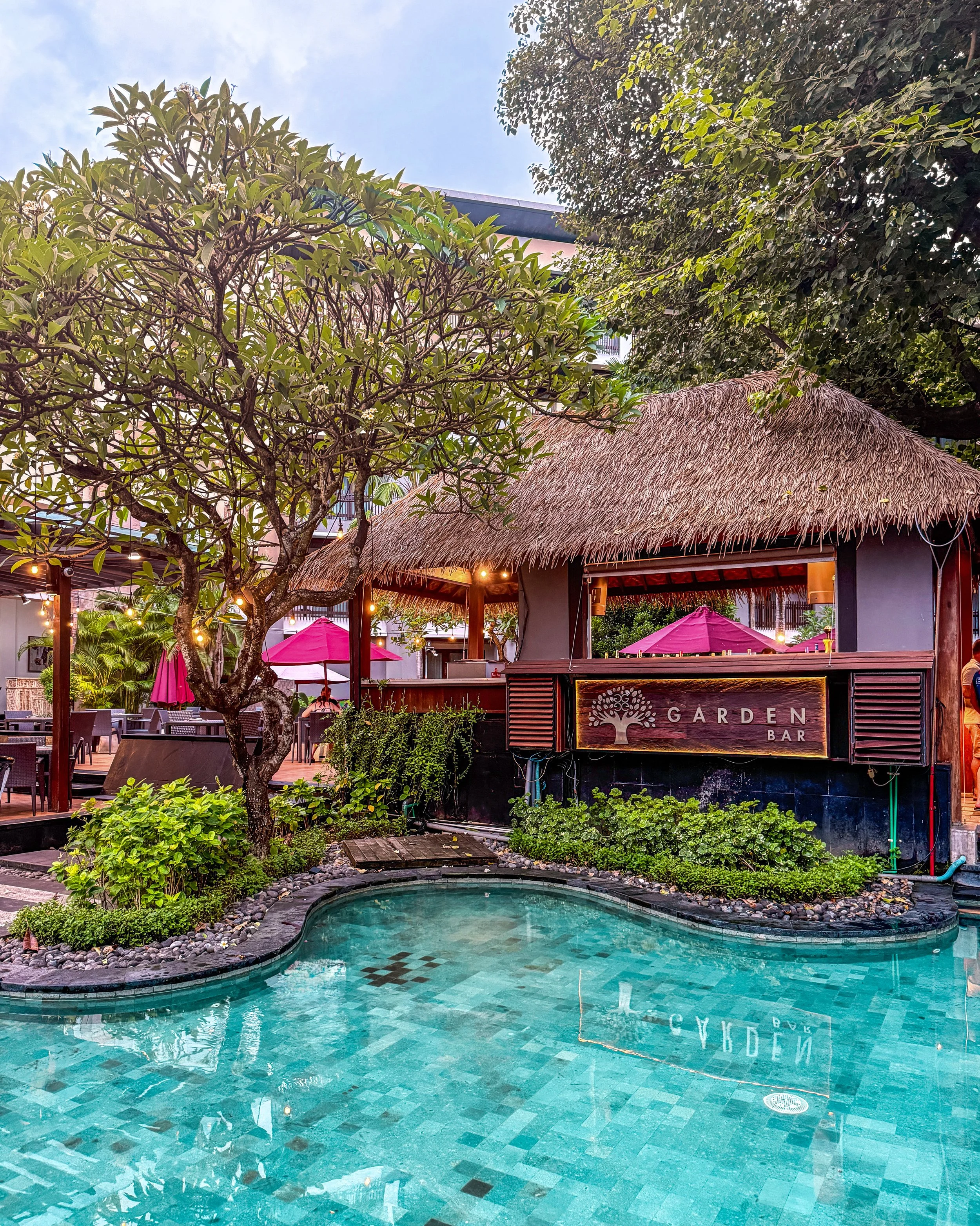 The Garden Bar overlooks a tranquil swimming pool framed by tropical gardens and traditional Balinese design