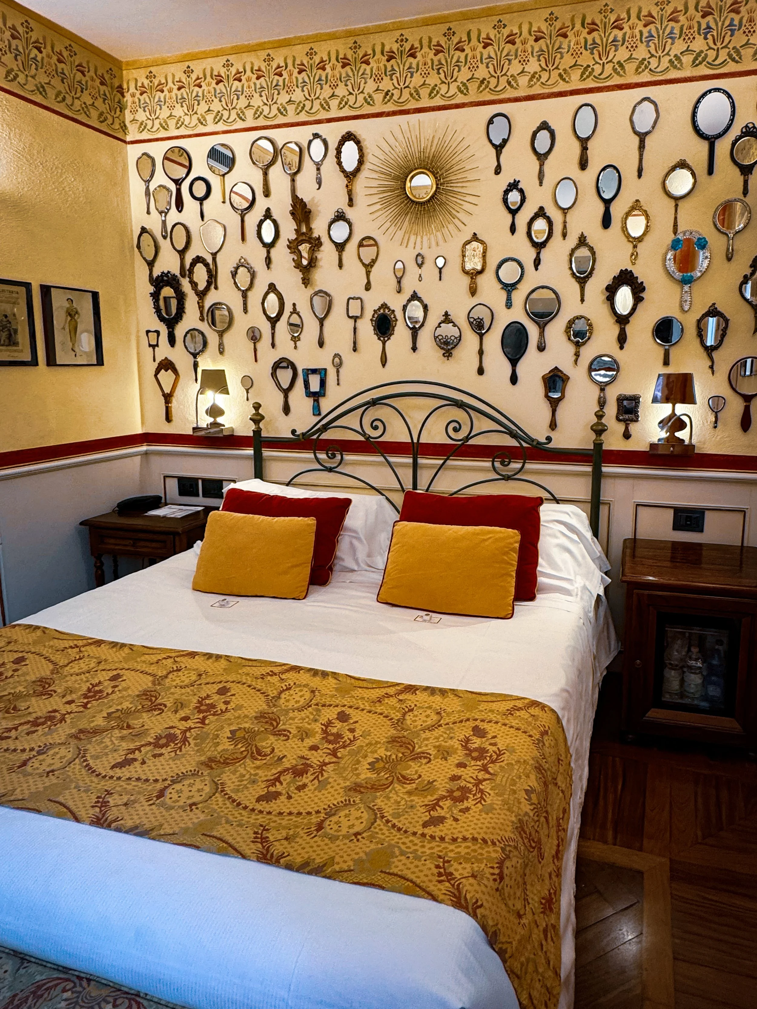 Double room with wrought iron headboard and decorative mirror wall feature, Art Hotel Commercianti – Bologna, Italy.