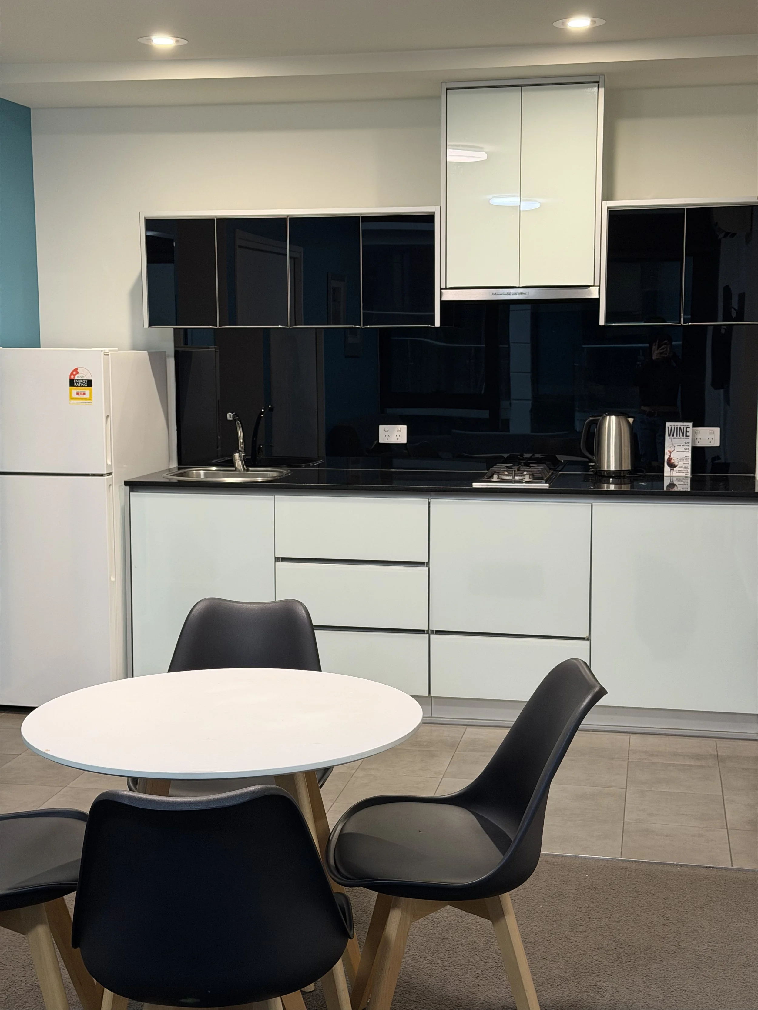 Fully equipped apartment kitchenette featuring white cabinetry, black backsplash, refrigerator, stovetop, and dining area