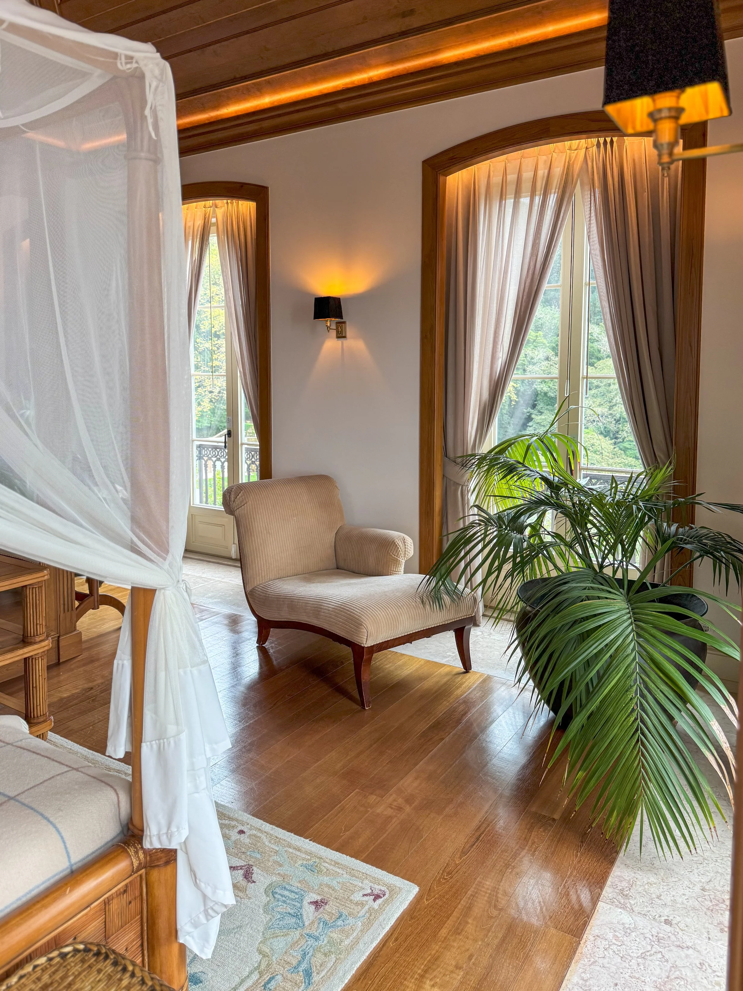 A bright bedroom pairs a canopy bed, warm wood floors, and garden-facing windows