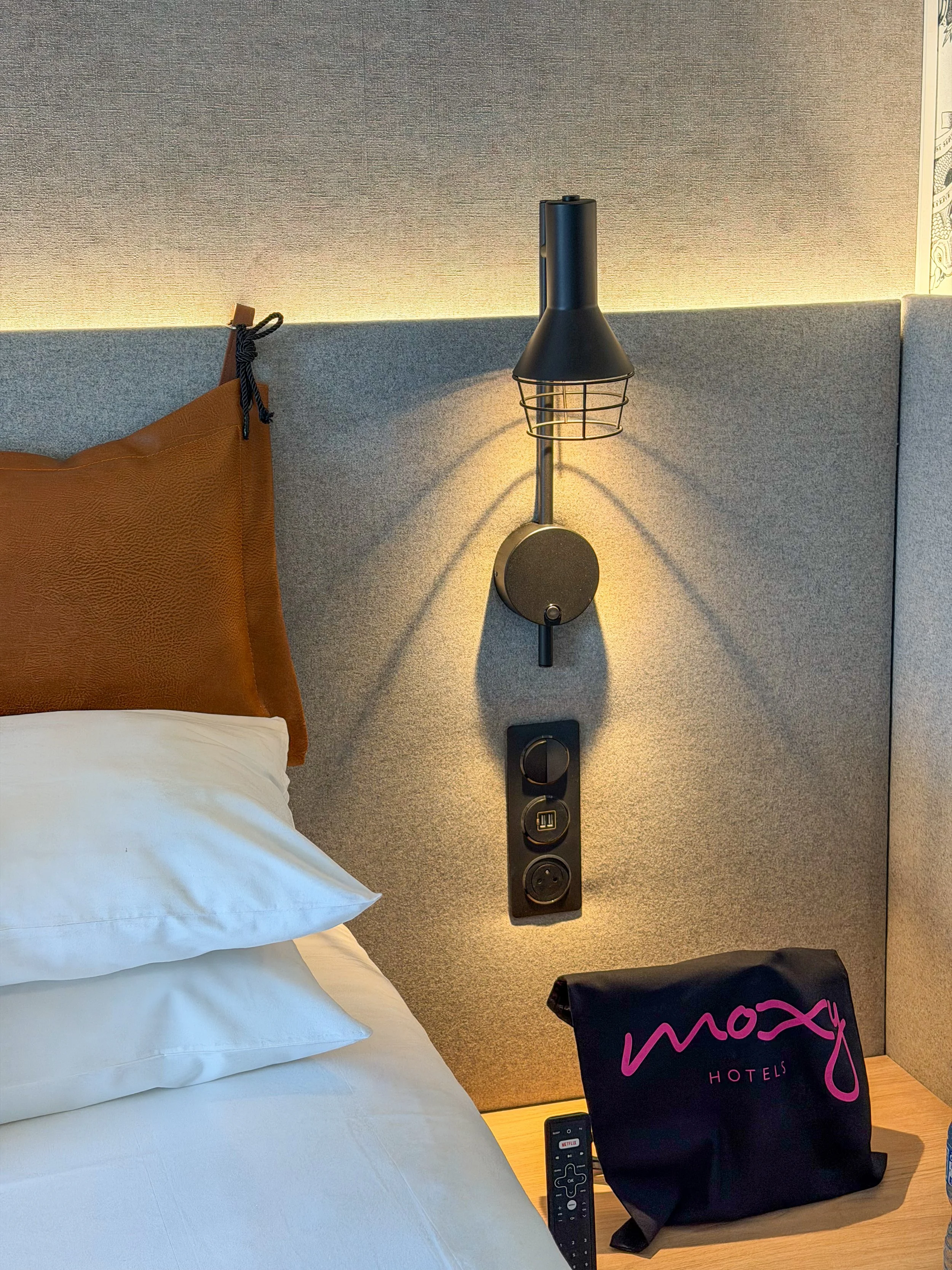 Minimalist guest room detail with bedside lighting, leather accents, and Moxy amenities