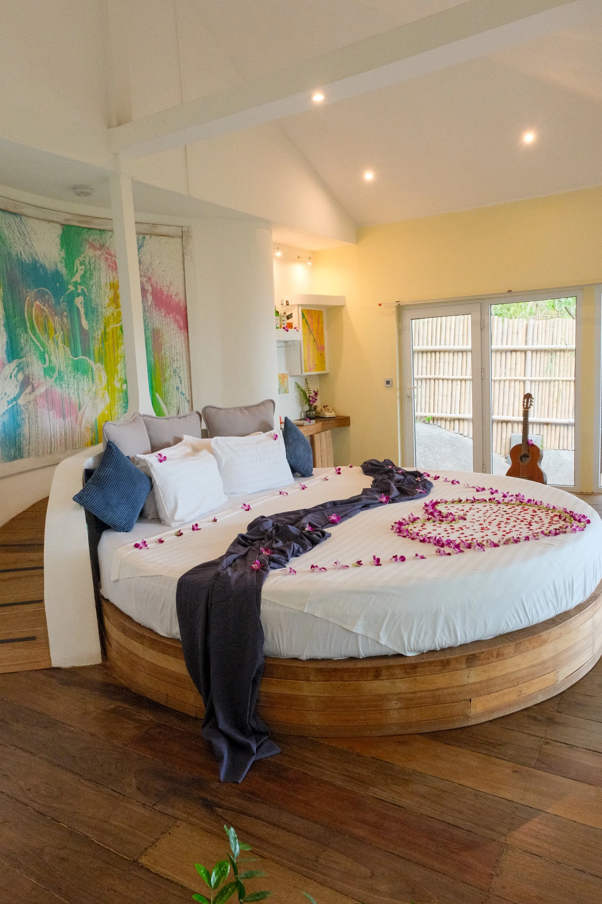 Circular bed decorated with tropical flowers, colorful artwork, warm wooden floors, and a bright contemporary interior