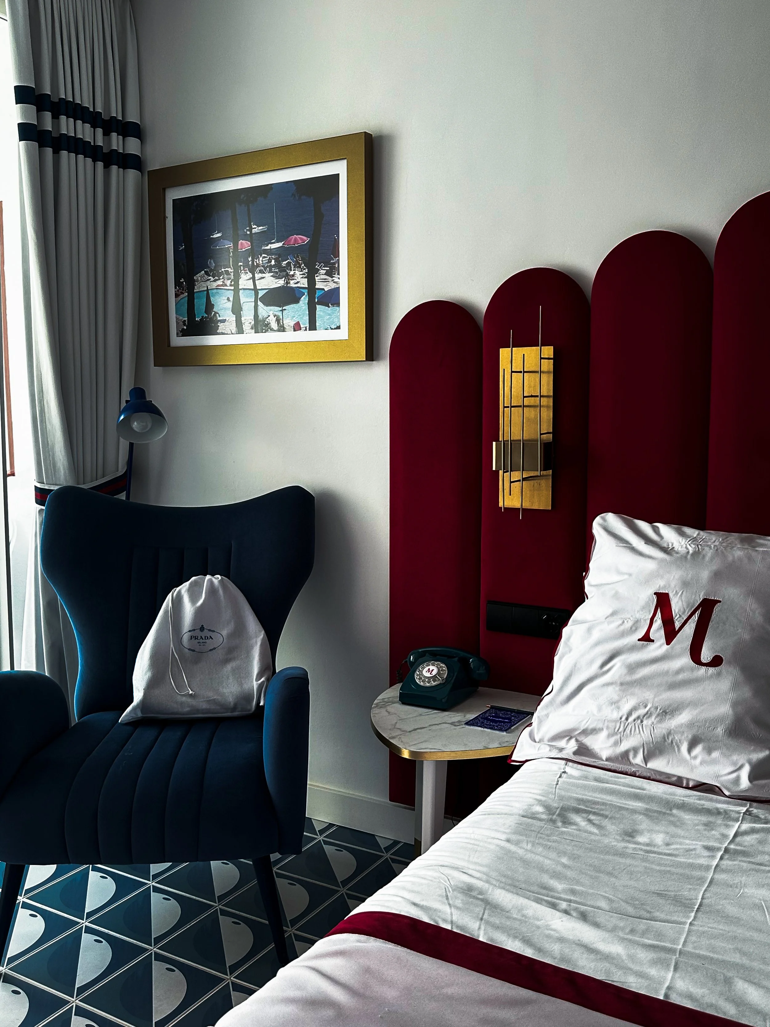 Stylish guest room featuring a burgundy velvet headboard, blue armchair, vintage telephone, and Mediterranean-inspired furnishings