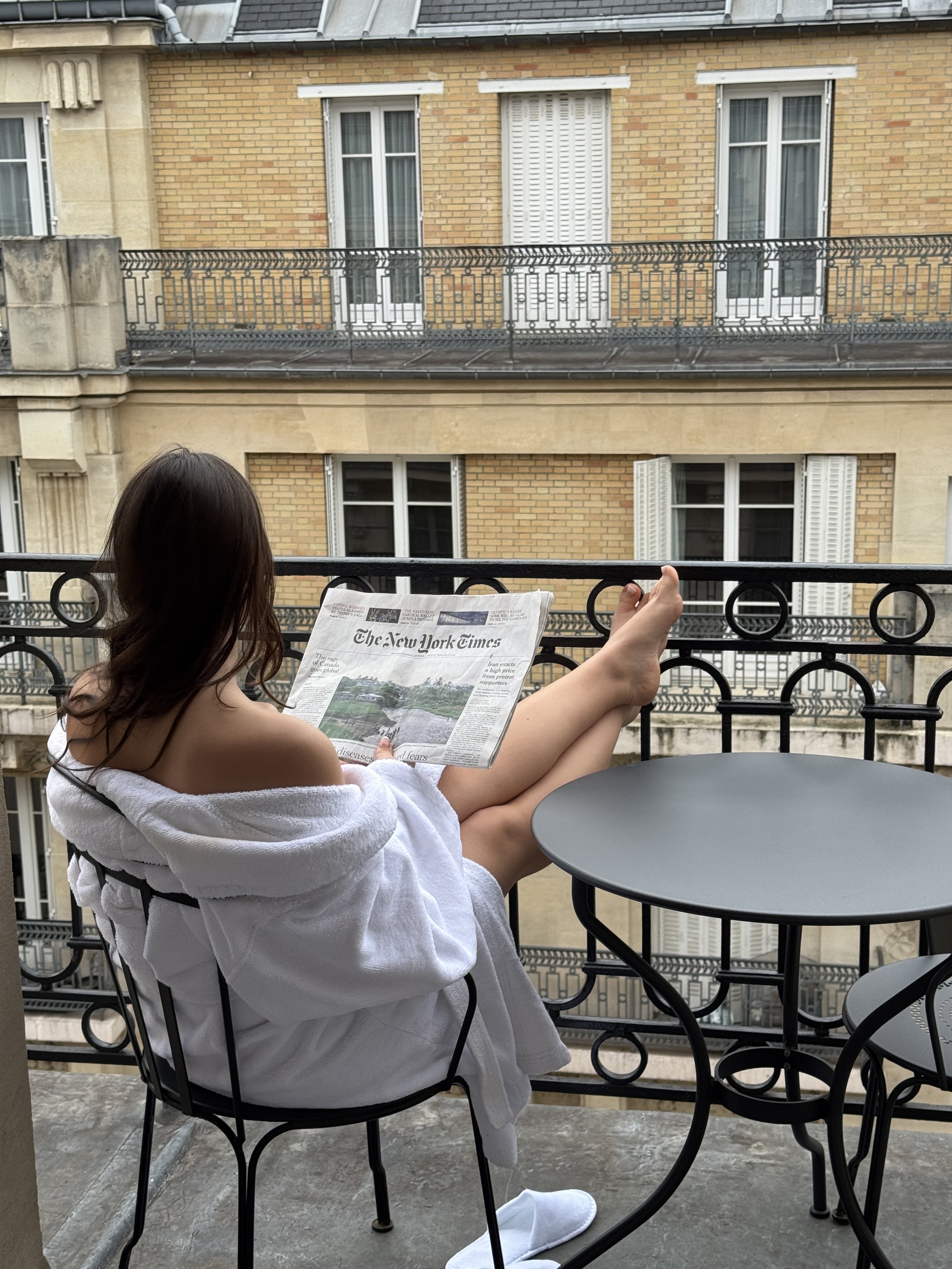 Guest relaxing on a wrought-iron balcony reading a newspaper overlooking traditional Parisian buildings, Victoria Palace Hotel – Paris, France.