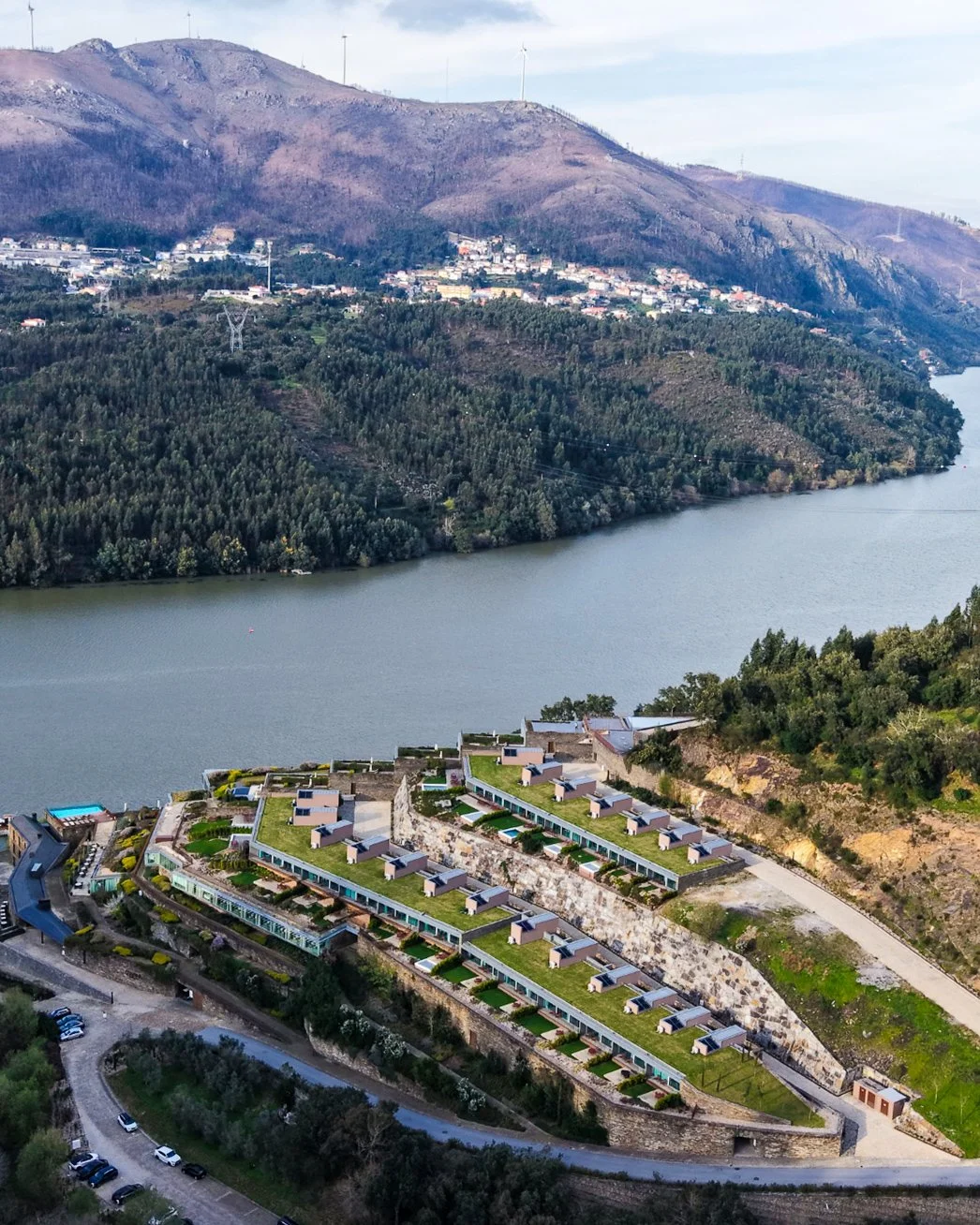 Aerial view of terraced suites cascading down the hillside with green roofs and river views in the Douro Valley, Octant Douro – Castelo de Paiva, Portugal.