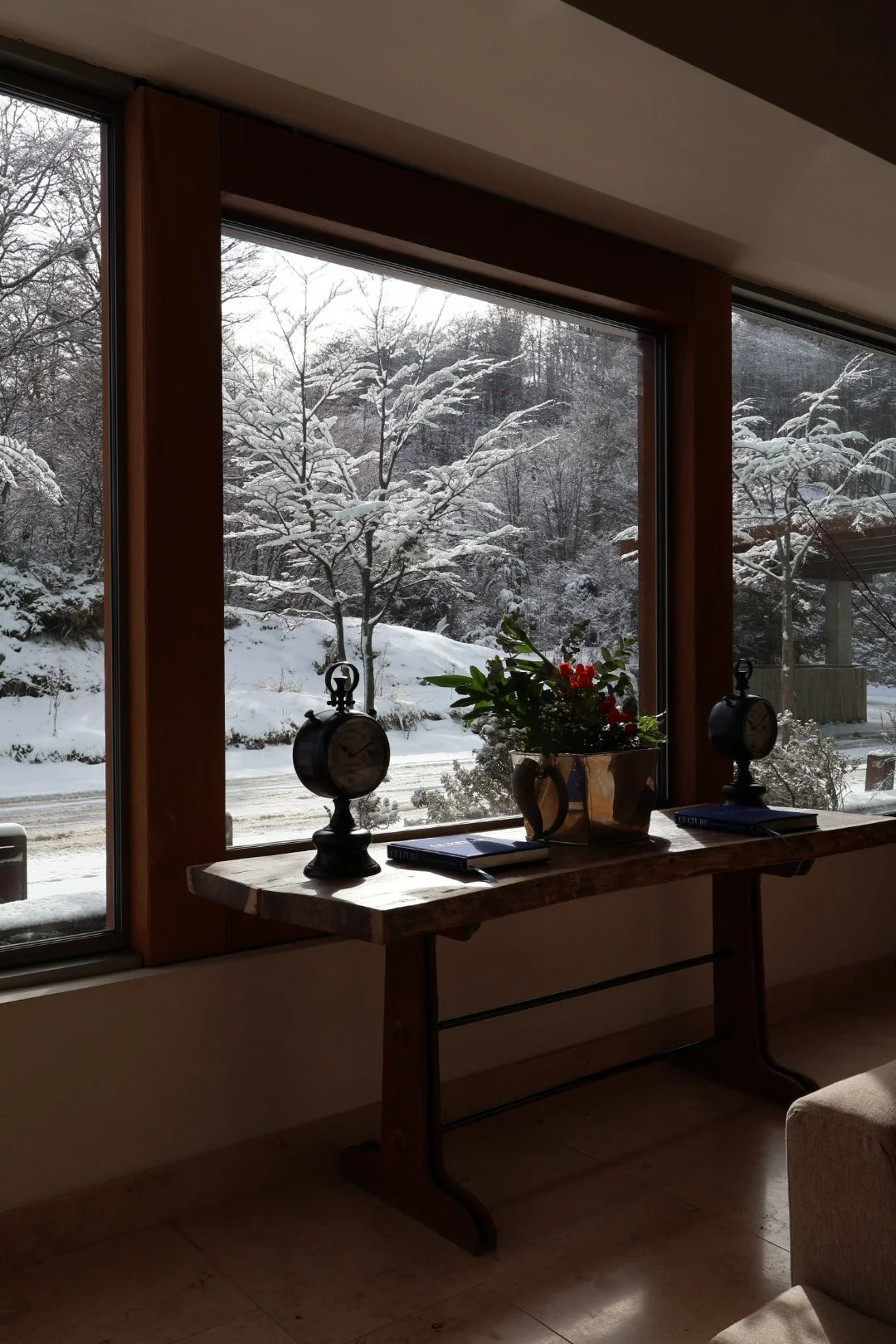 Snow-covered Patagonian forest viewed through large windows beside rustic wood furnishings and floral details