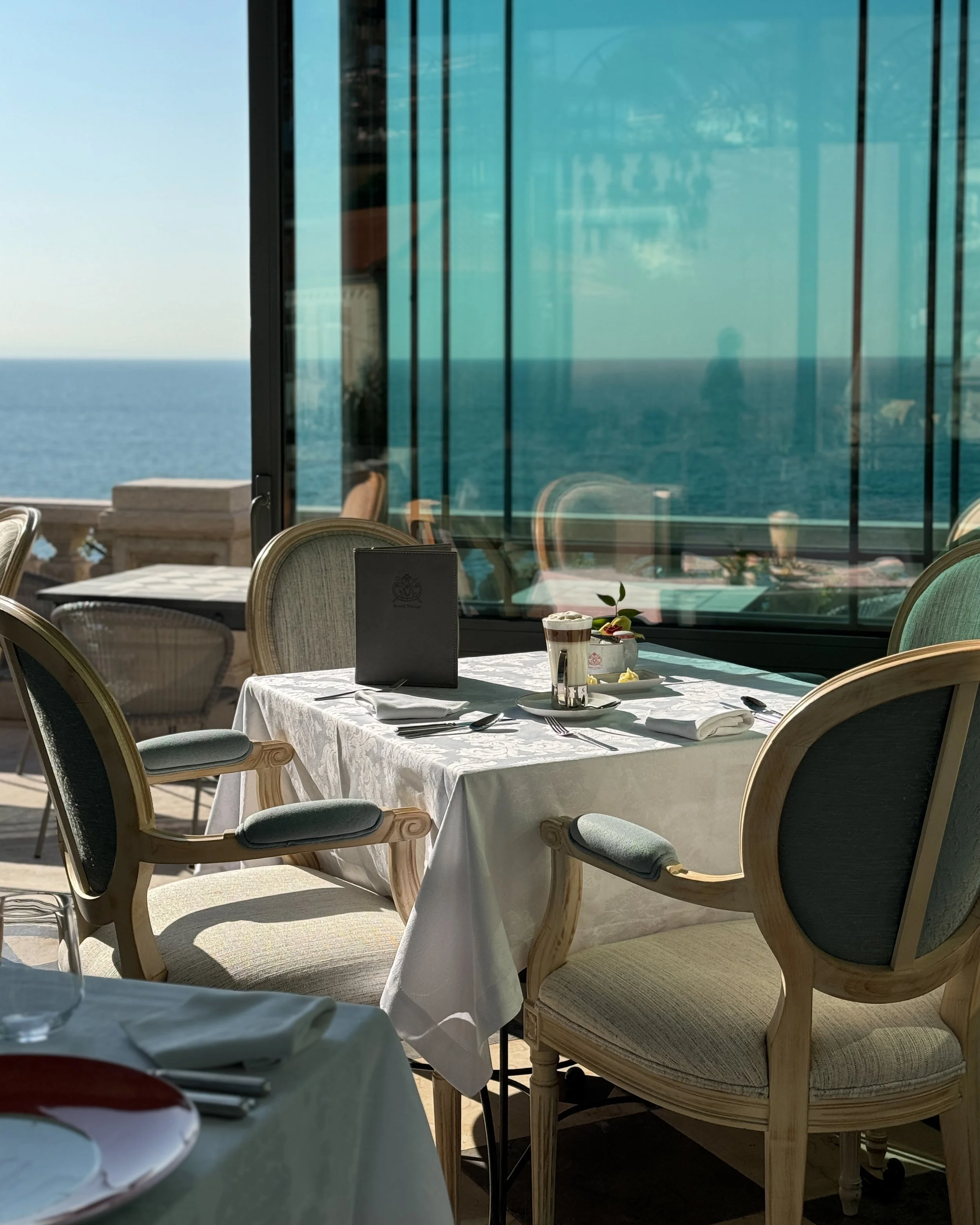 Refined dining setting with ocean views, crisp linens, and soft daylight reflecting off the water, Estoril Vintage Hotel – Estoril, Portugal.