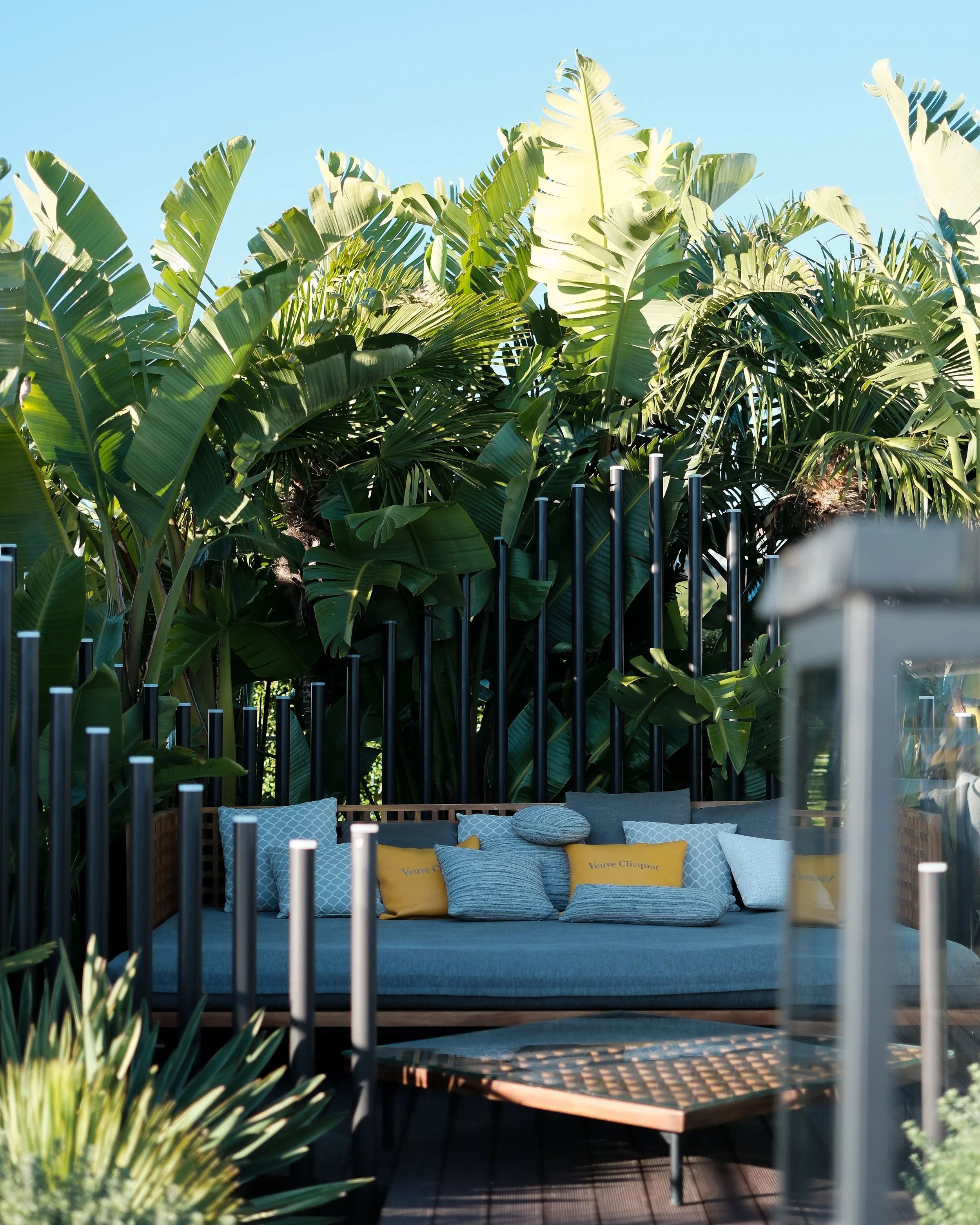 Tropical rooftop seating area with oversized palm leaves, shaded cushions, and a serene open-air atmosphere — Hyatt Regency Lisbon