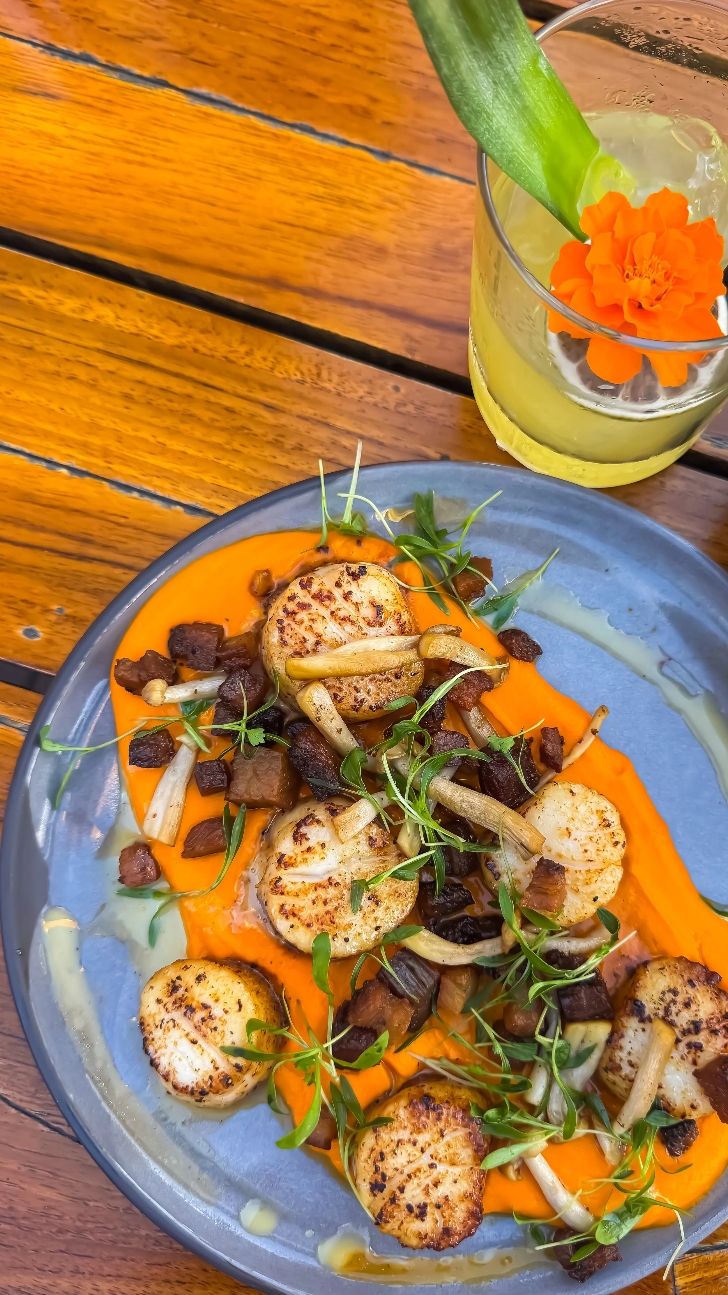 Pan-seared scallops served with seasonal vegetables and vibrant purée alongside a handcrafted cocktail