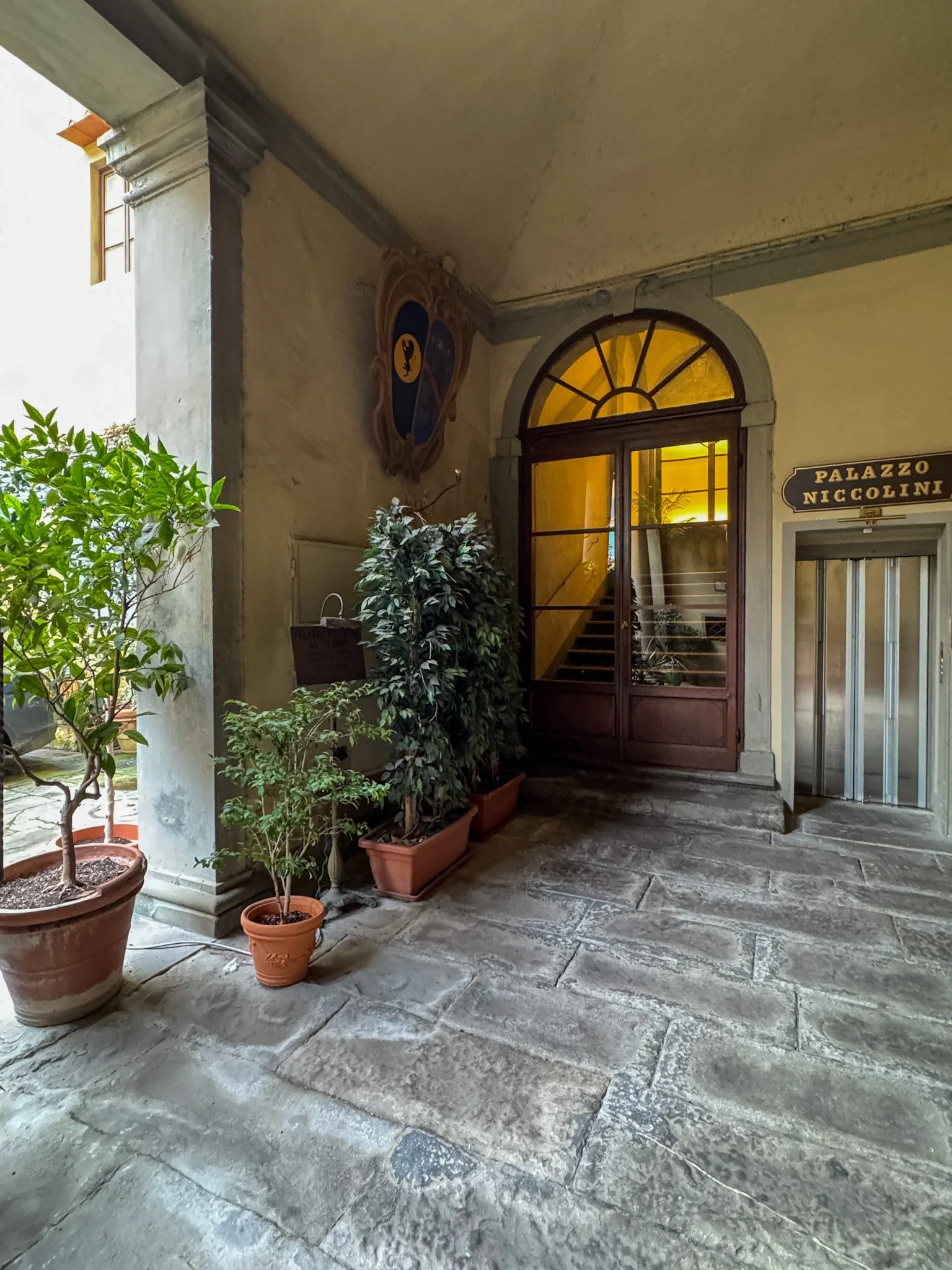 Historic entrance courtyard with stone floors, potted plants, and arched doorway, Palazzo Niccolini al Duomo – Florence, Italy.