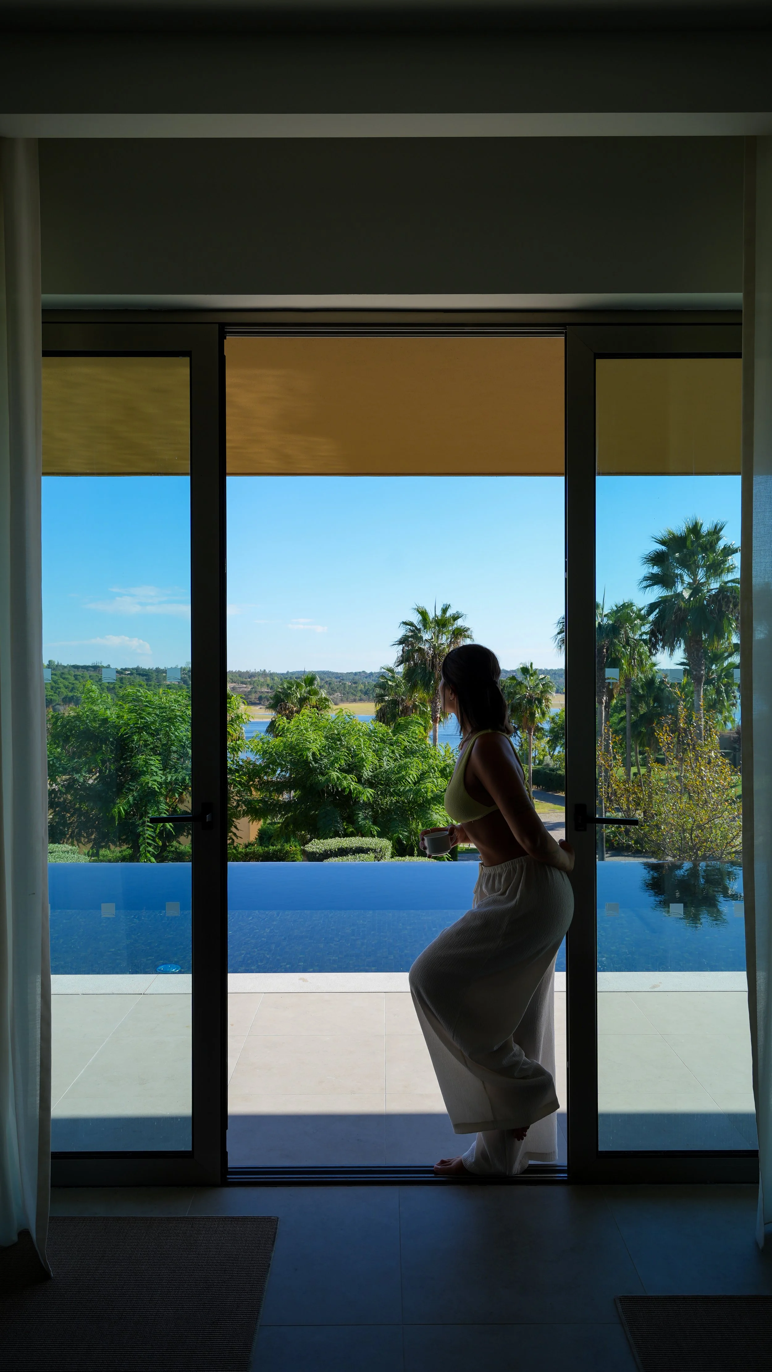 Guest enjoying a peaceful morning beside a private infinity pool with panoramic lake and palm tree views