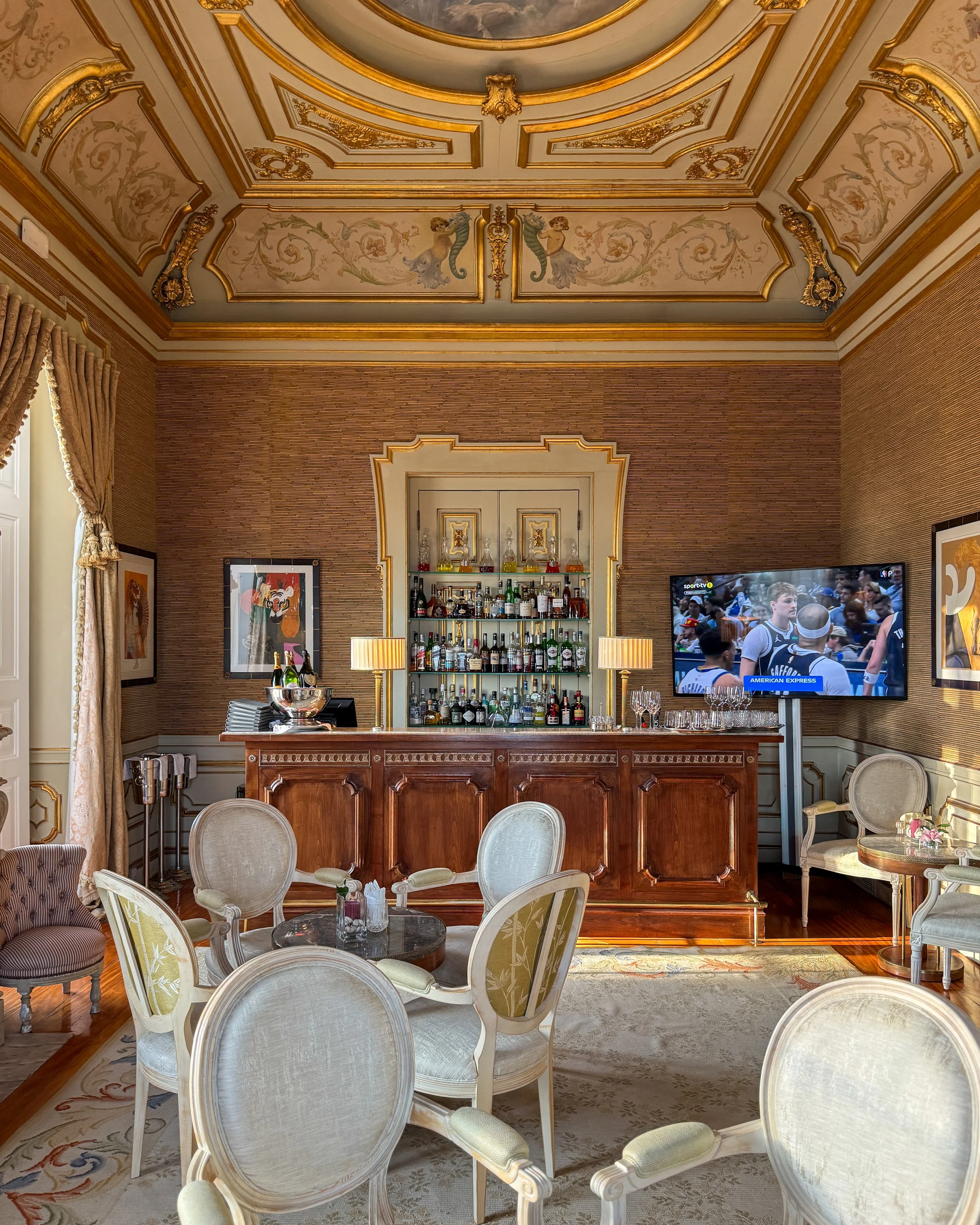 Ornate bar lounge with gilded ceiling, classic furnishings, and warm light highlighting timeless interiors, Estoril Vintage Hotel – Estoril, Portugal.