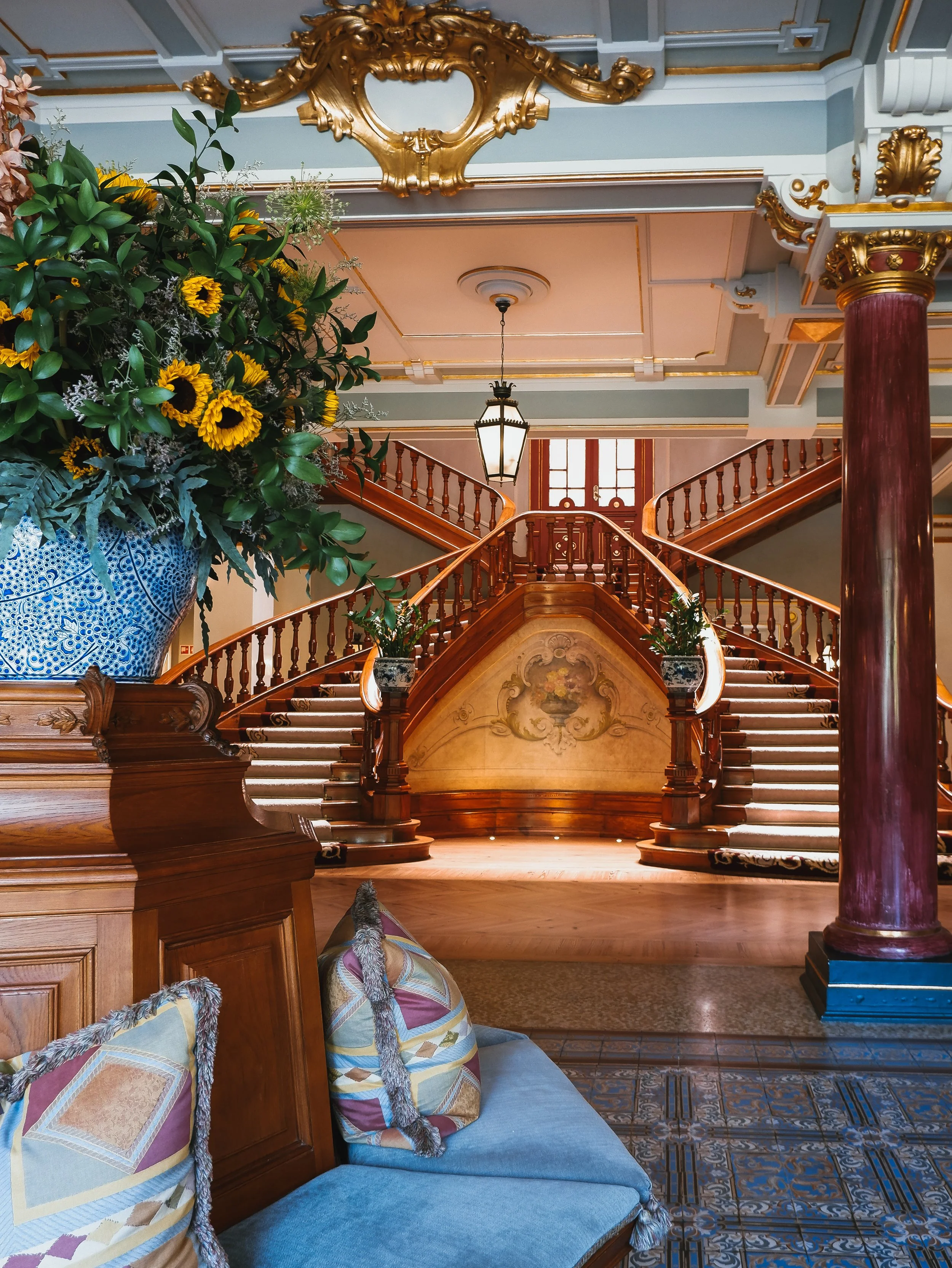 Luxury hotel lobby featuring an iconic sweeping staircase, ornate details, and fresh floral arrangements