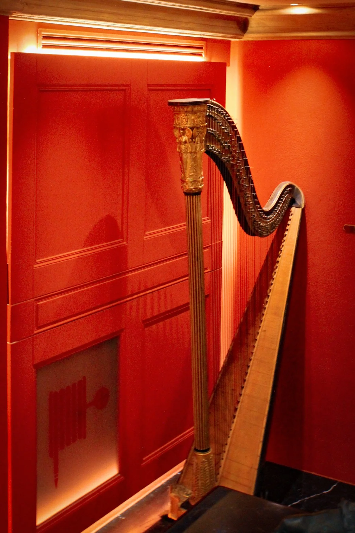 Classic harp displayed against bold red walls in intimate hotel corner, Art Hotel Commercianti – Bologna, Italy.