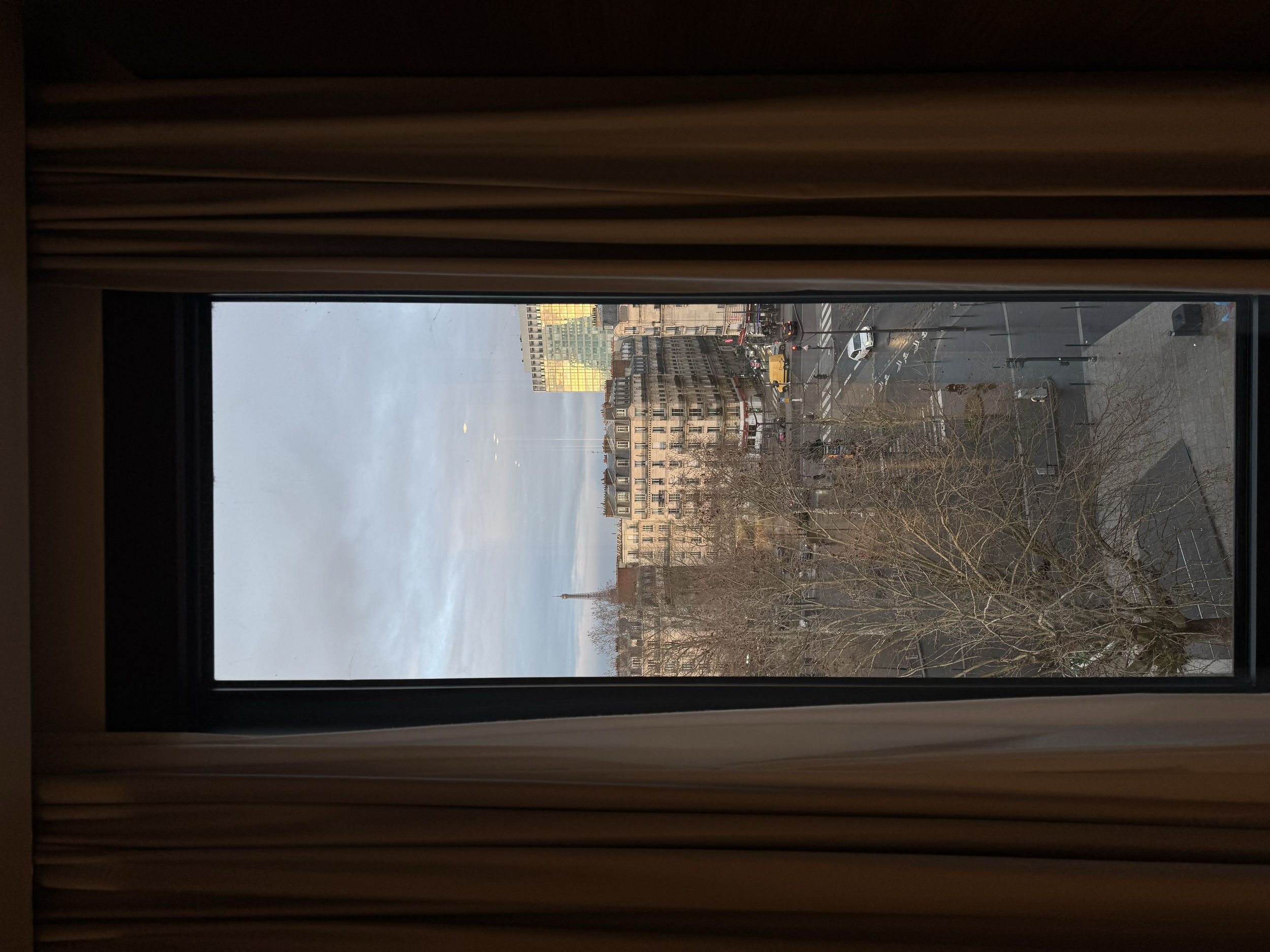 Framed city view from a guest room window with classic Parisian buildings and distant skyline, Novotel Paris Porte de Versailles – Paris, France.