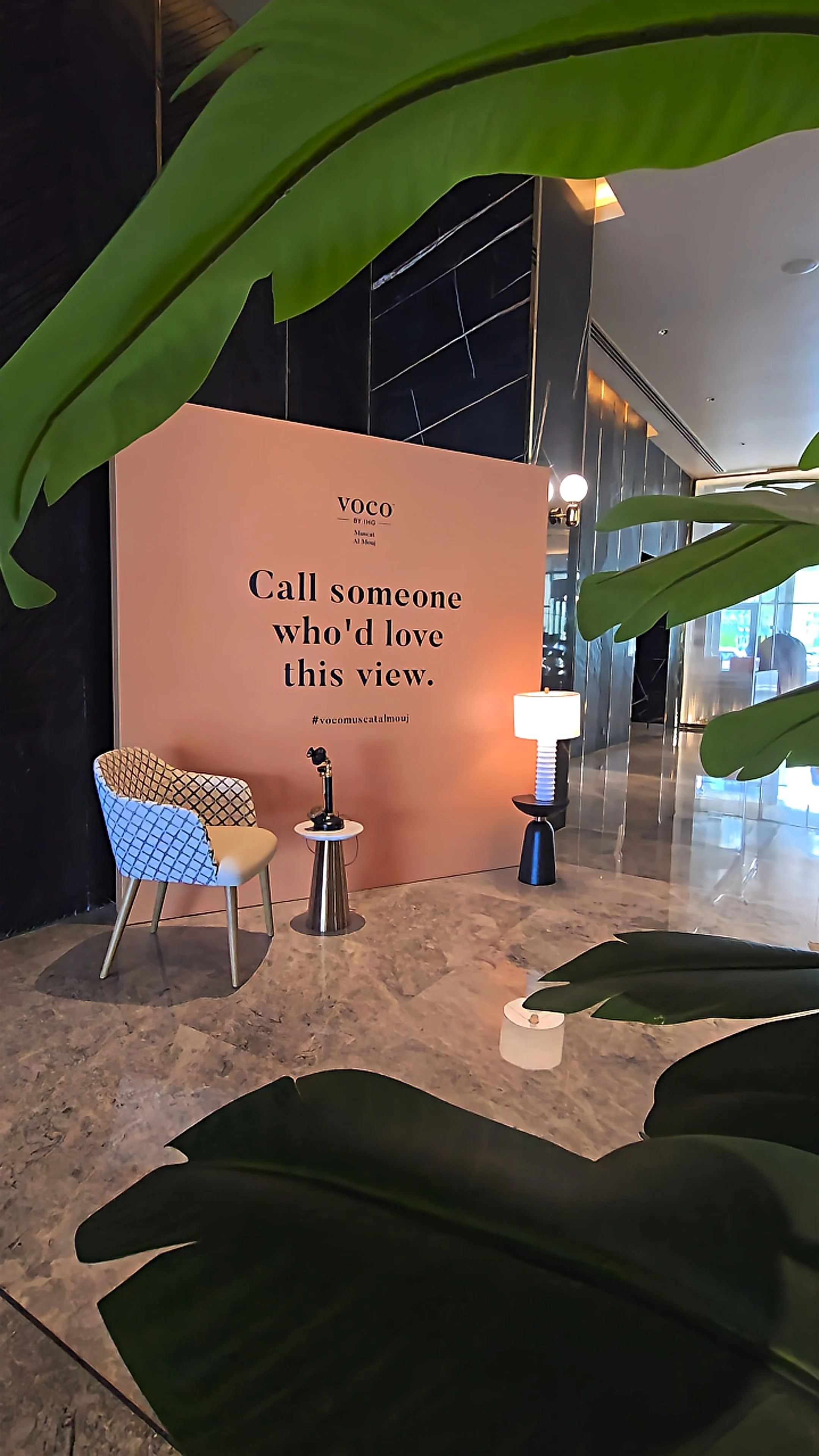 Stylish hotel lobby with a decorative pink feature wall, contemporary seating, tropical plants, and marble flooring