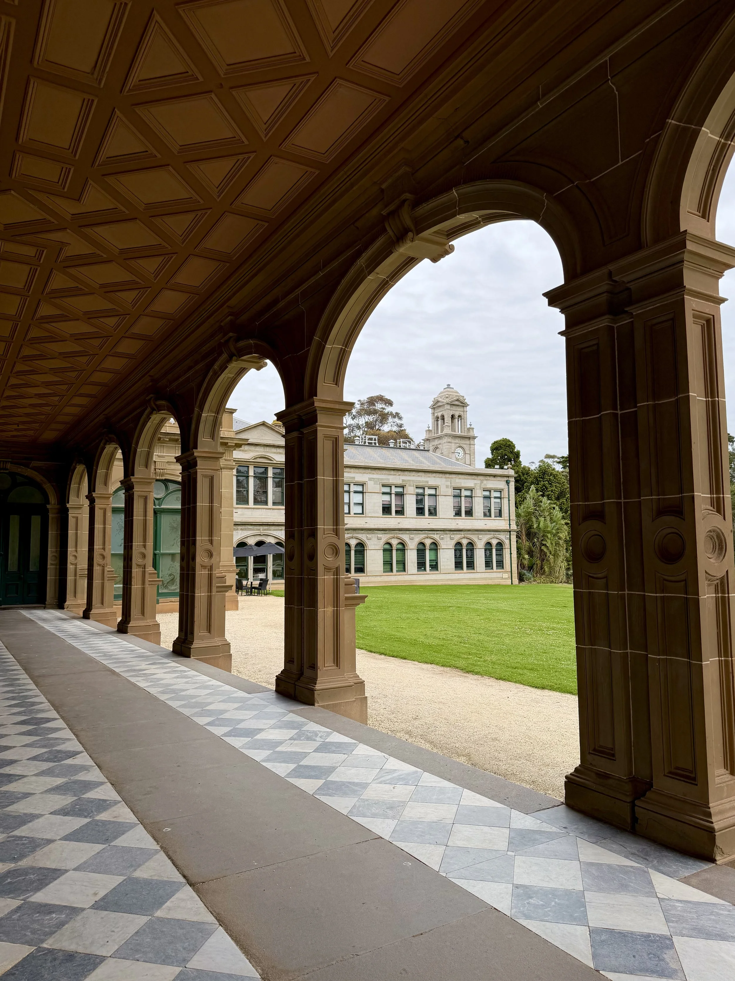 Historic sandstone archway overlooking the mansion's clock tower, manicured lawns, and surrounding gardens