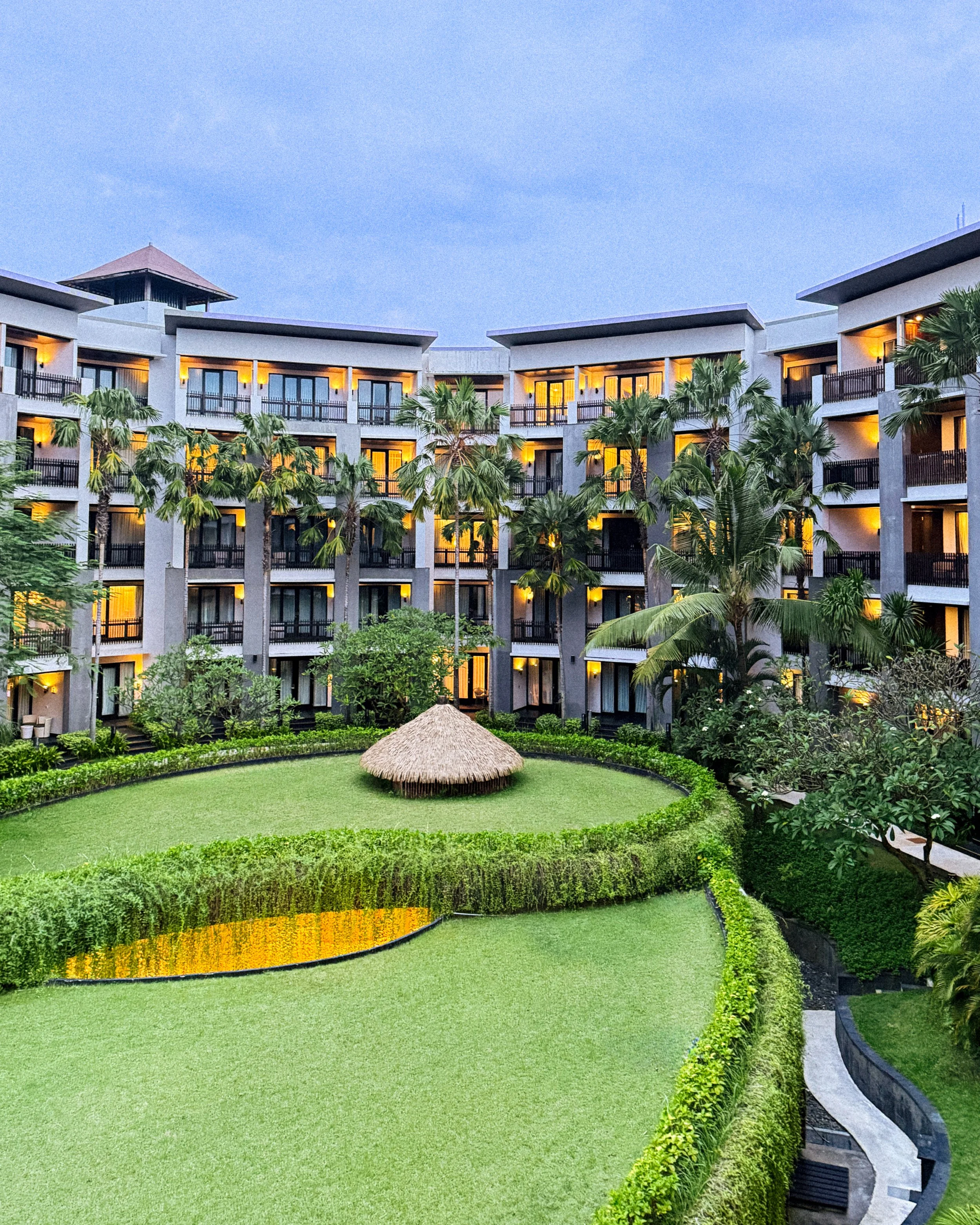 Lush courtyard with tropical landscaping and illuminated balconies at Pullman Bali Legian Beach